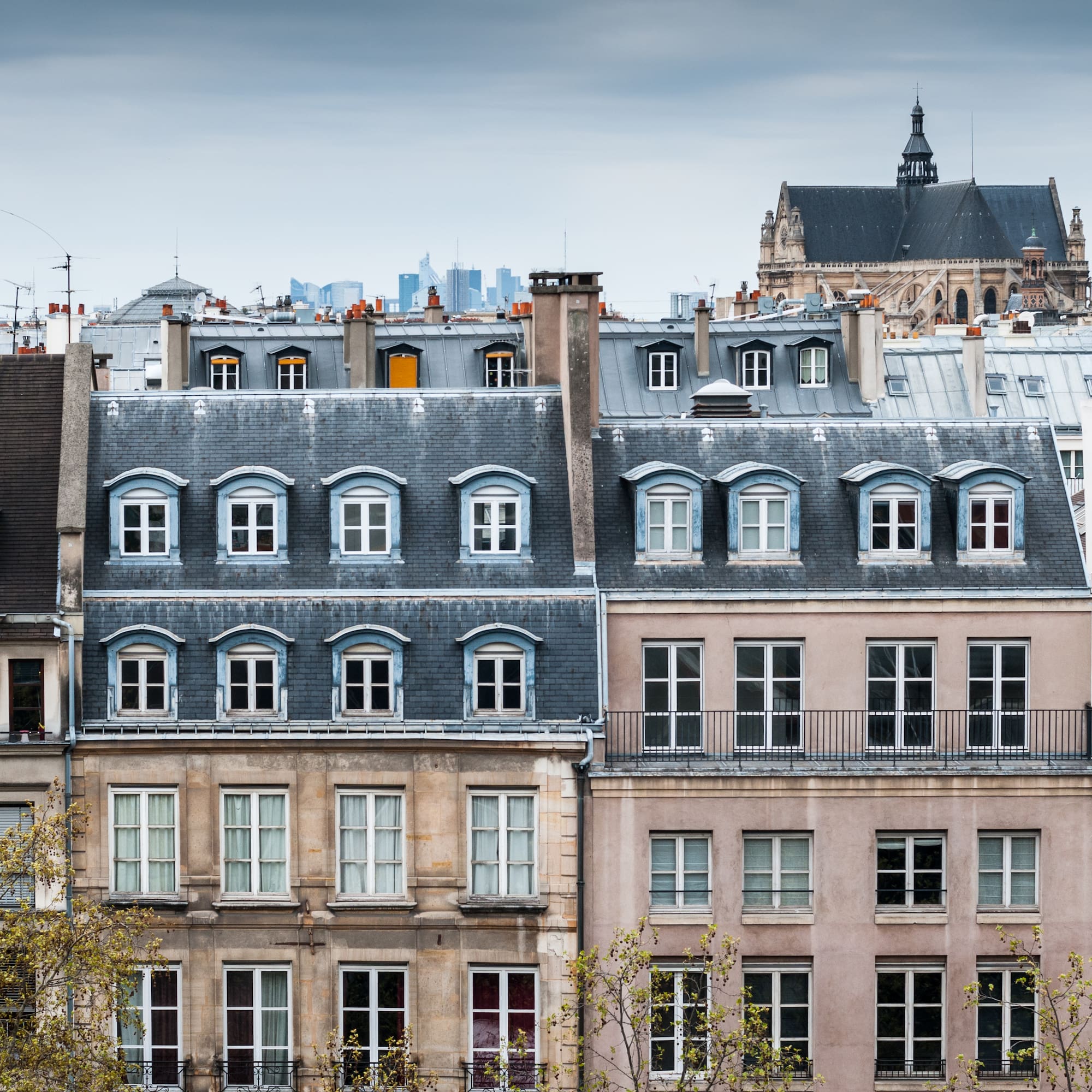 Edificios parisinos con tejados de pizarra, buhardillas y torre de iglesia al fondo.