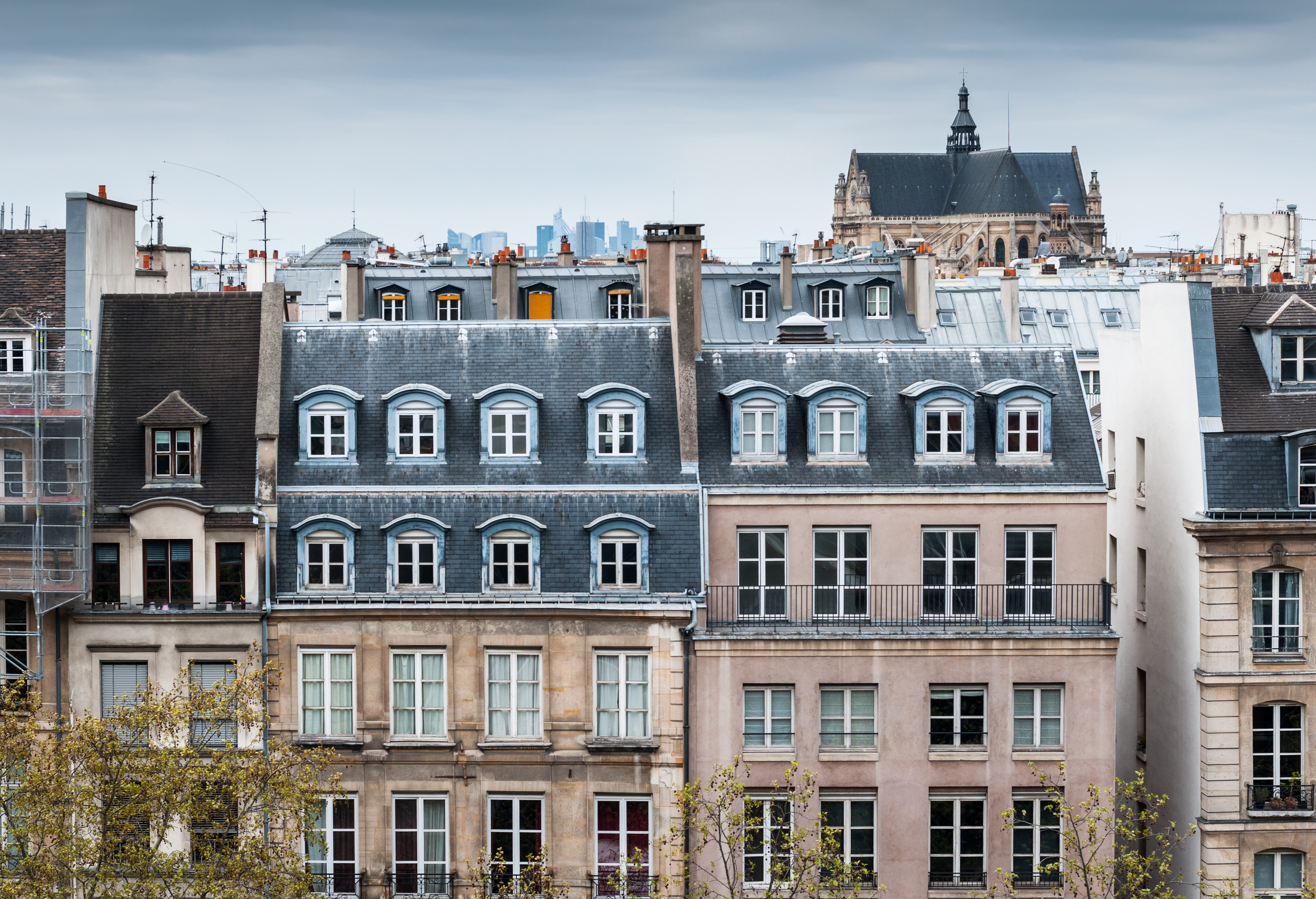 Edificios parisinos con tejados de pizarra, buhardillas y torre de iglesia al fondo.