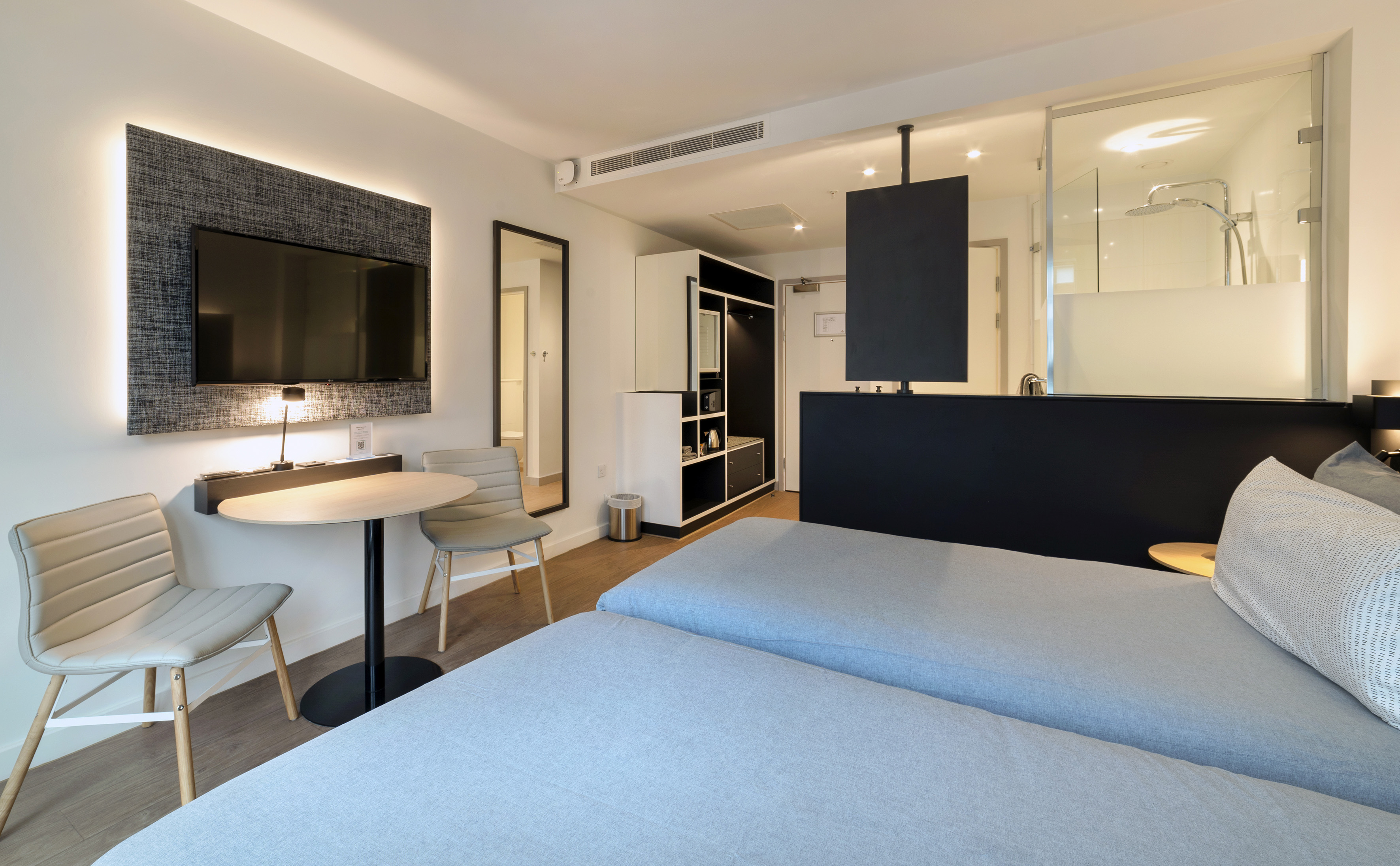 Modern hotel twin room with TV, work table, and glass shower.