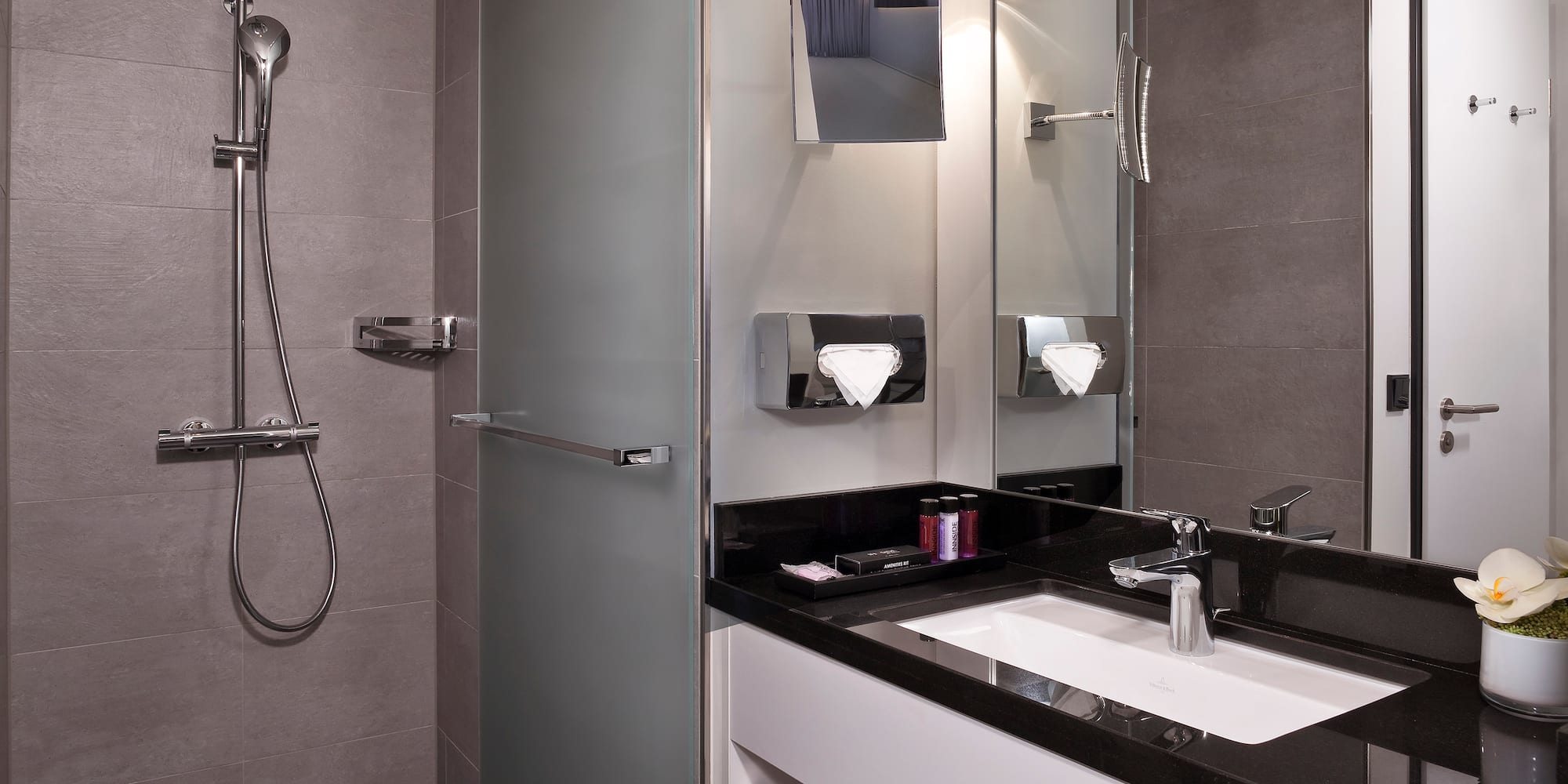 Modern bathroom with gray tiled shower, frosted glass partition, and black vanity.