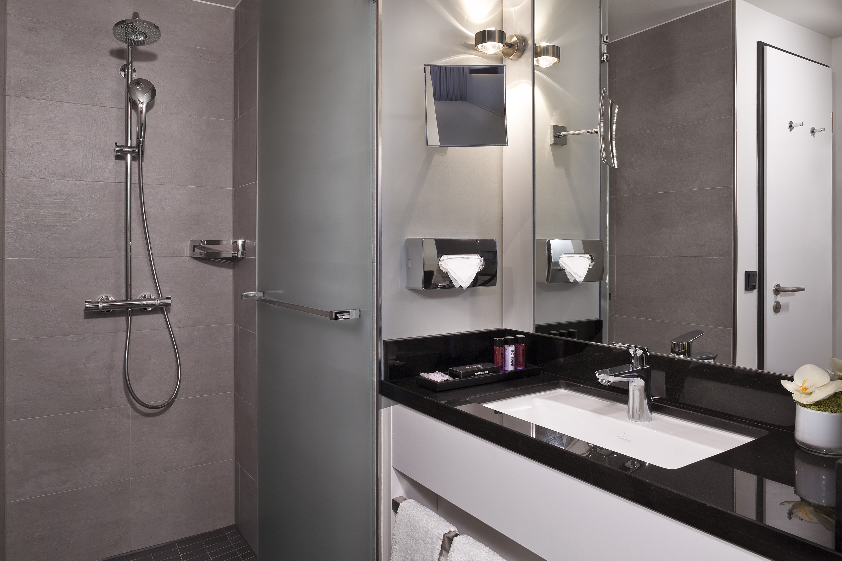 Modern bathroom with gray tiled shower, frosted glass partition, and black vanity.