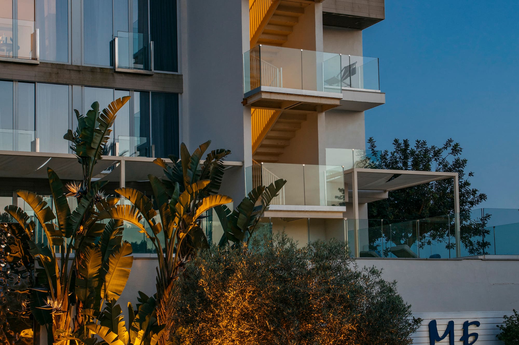 ME Ibiza hotel exterior at dusk, modern design with warm lighting and tropical plants.