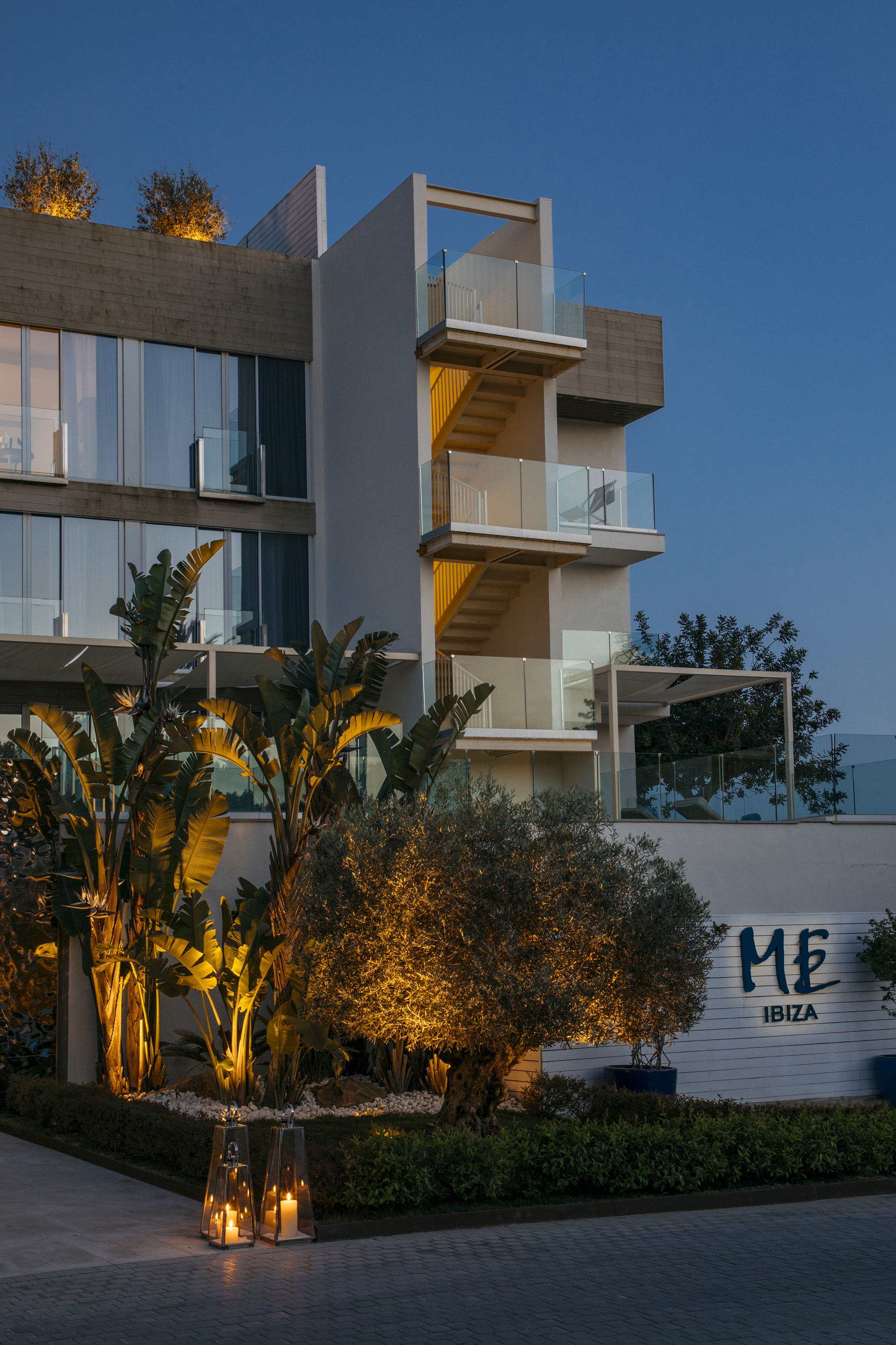 ME Ibiza hotel exterior at dusk, modern design with warm lighting and tropical plants.