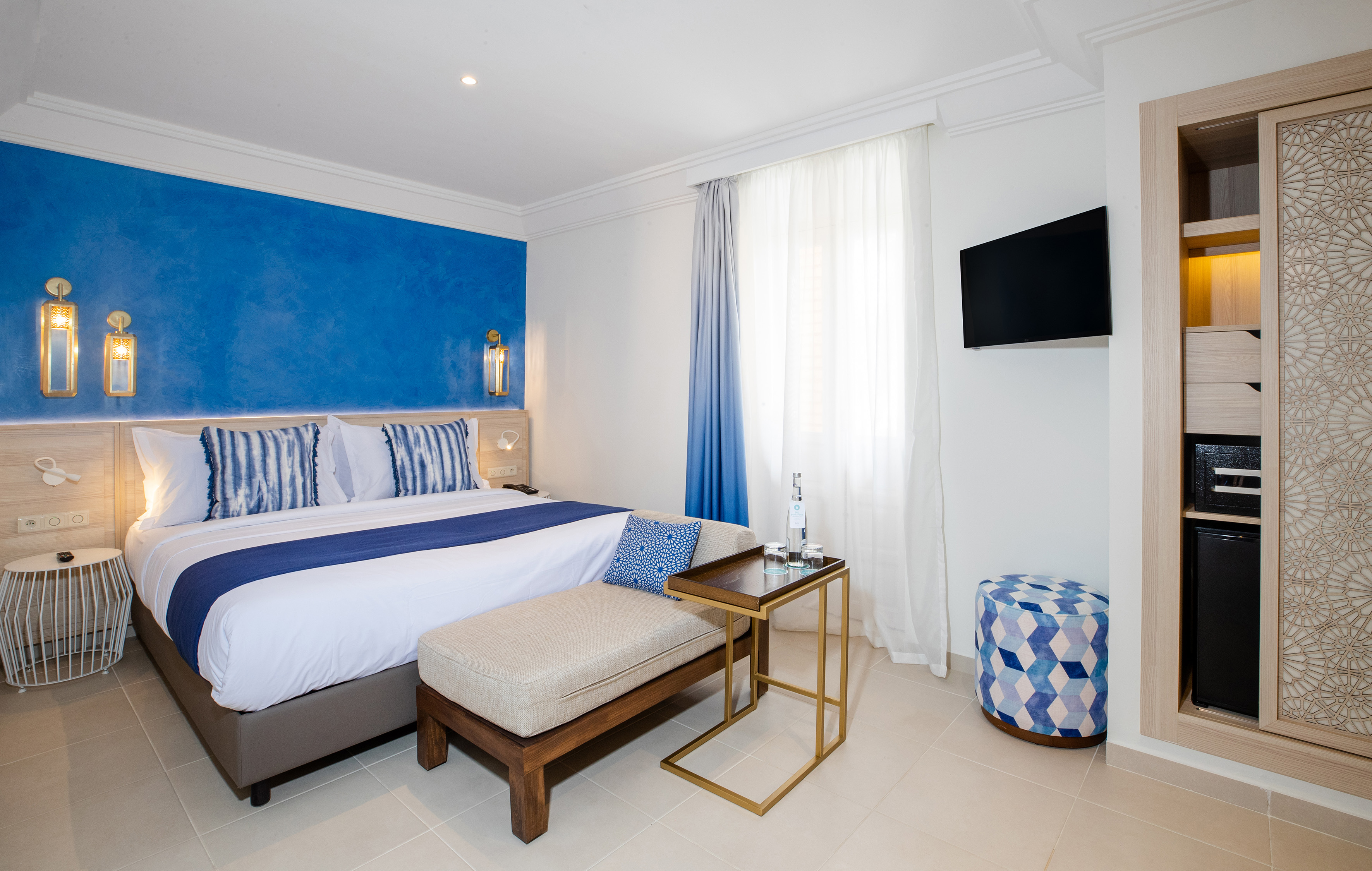 Modern hotel room with blue accent wall, bed, TV, and patterned wardrobe.