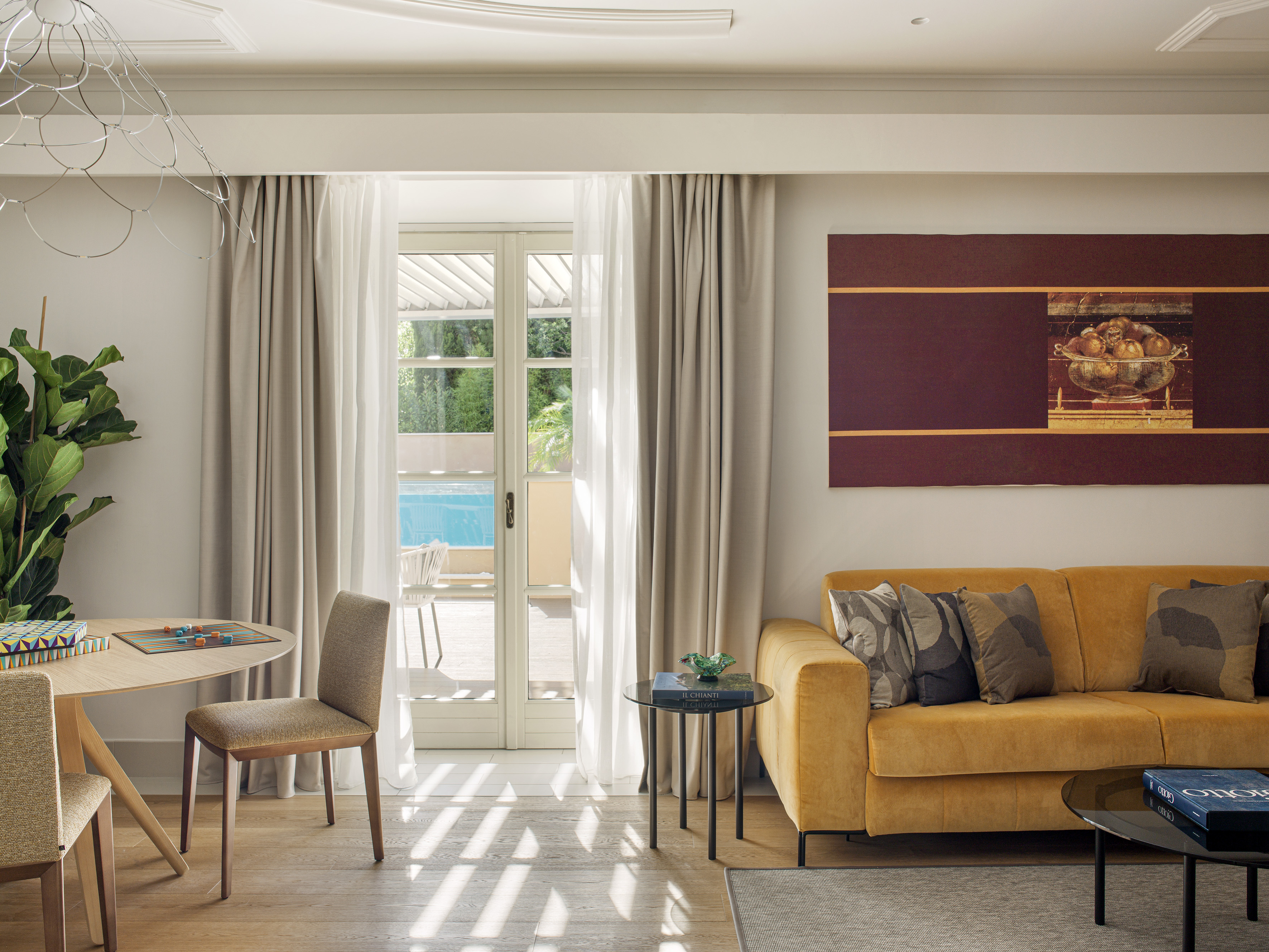 Elegant living room with yellow sofa, artwork, dining area, and pool view.