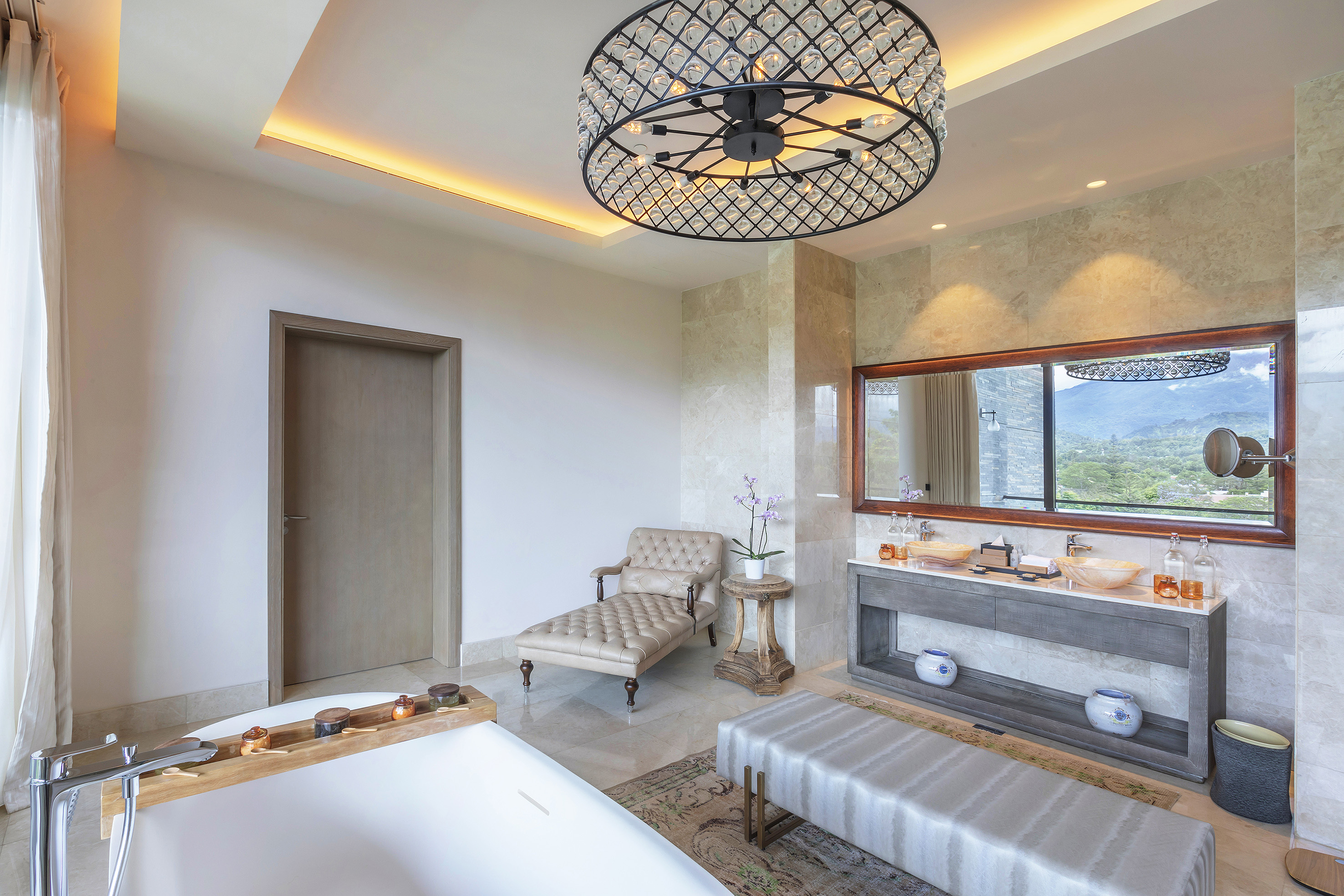 Luxury bathroom with crystal chandelier, freestanding tub, mountain view.