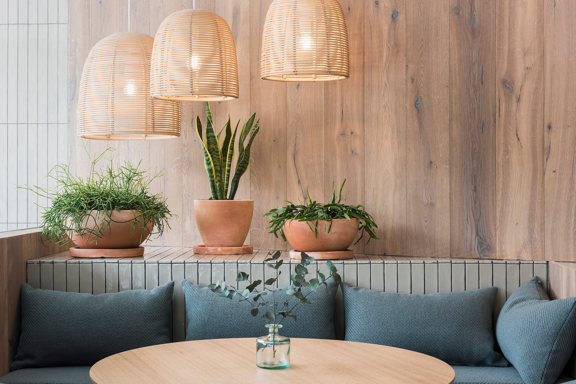 Cafe interior with rattan pendant lights, wood paneling, and potted plants.