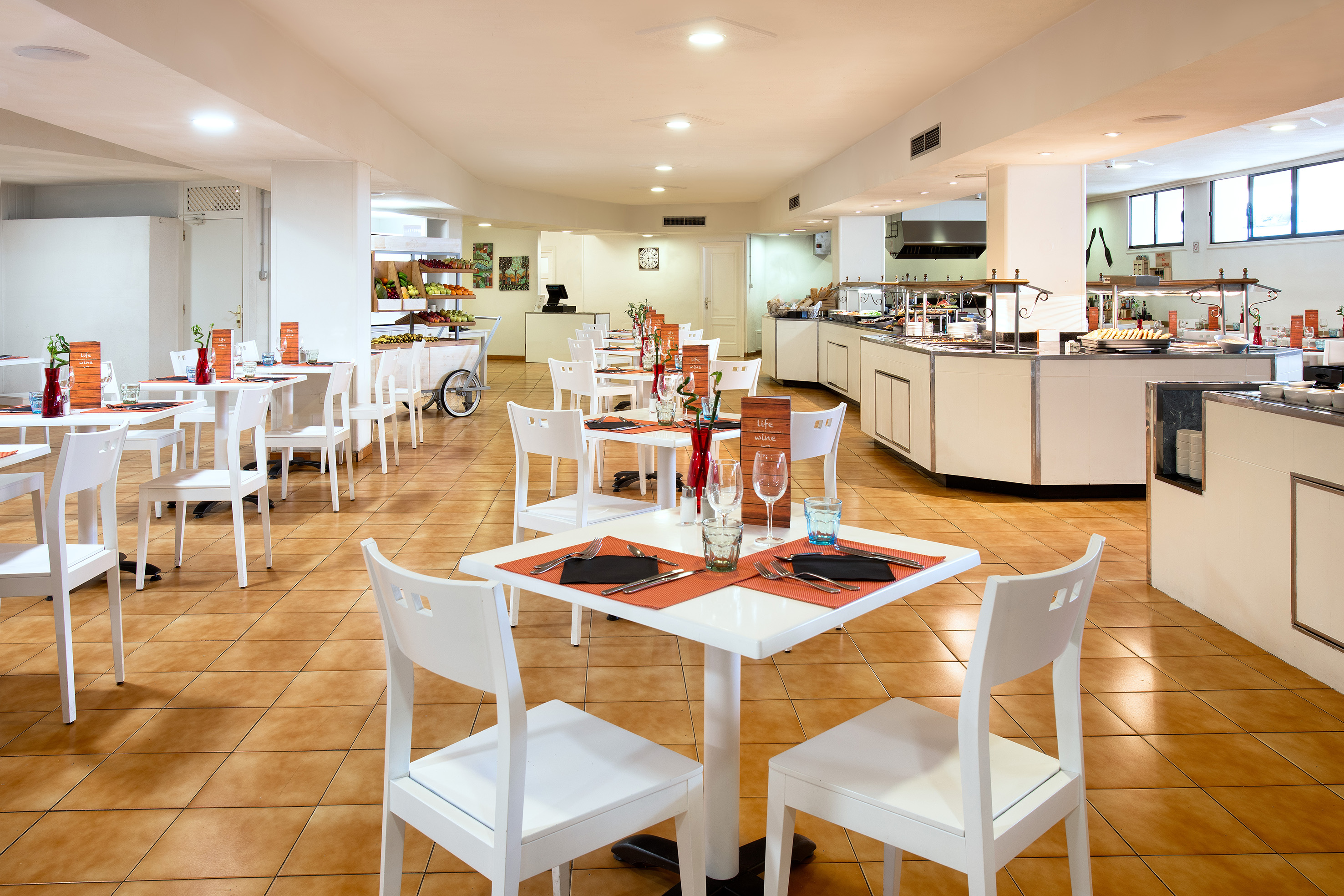 Bright hotel buffet restaurant with set tables, chairs, and fruit station.