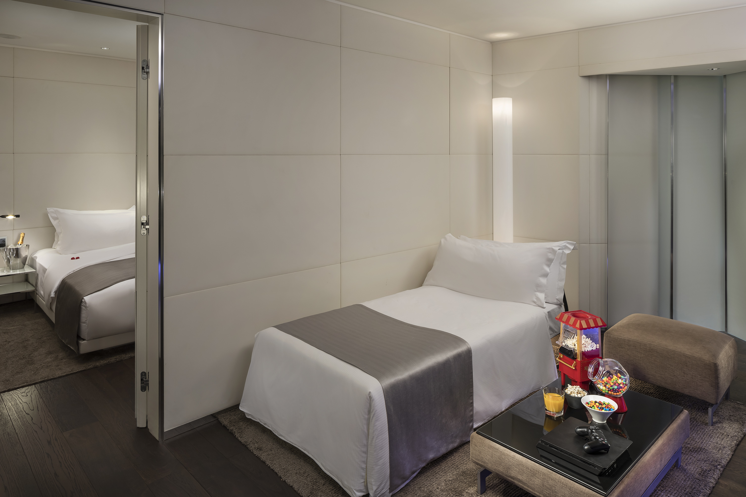 Modern hotel room with single bed, gaming console, popcorn, and snacks.