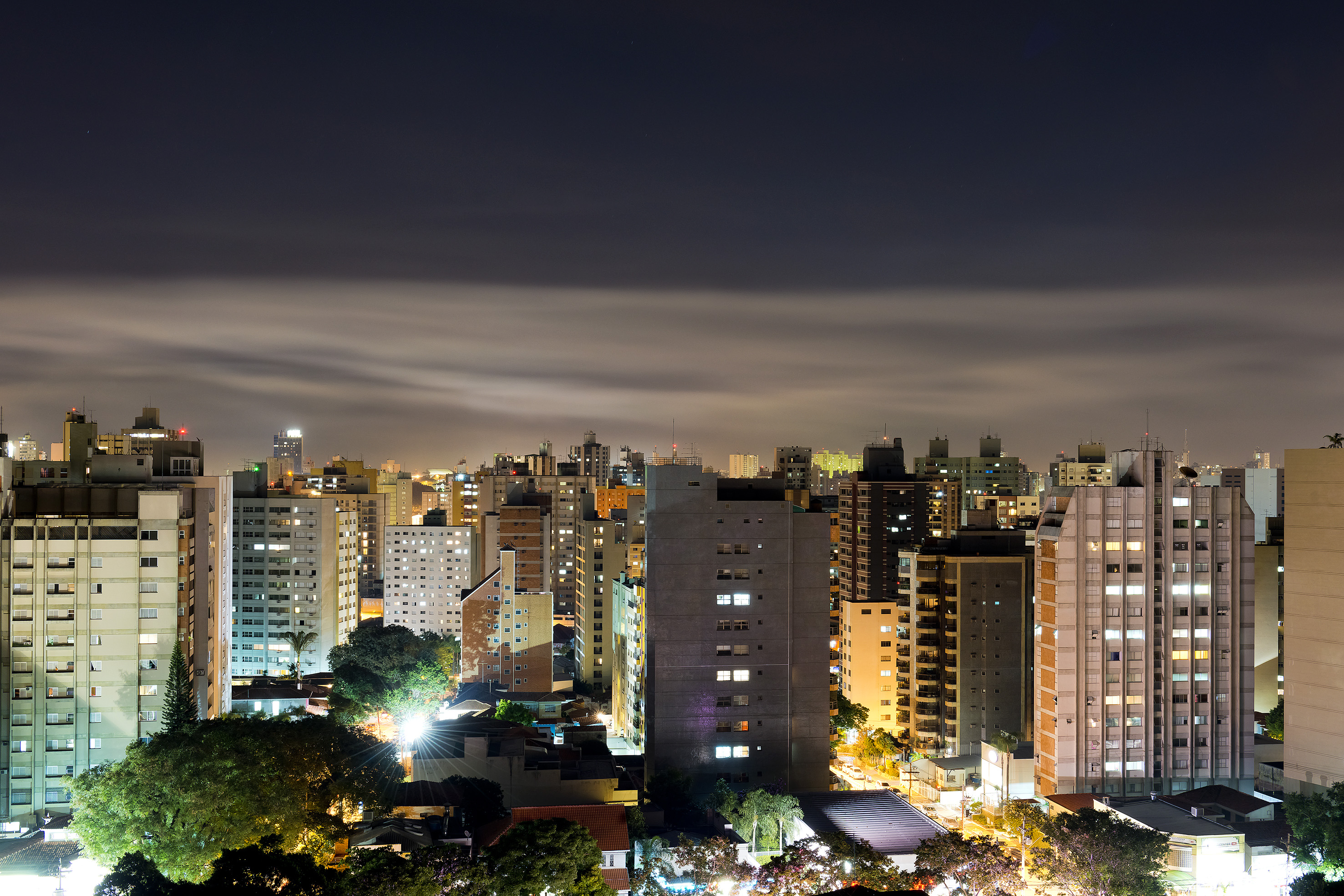 Night city skyline with illuminated buildings and streaky clouds overhead.