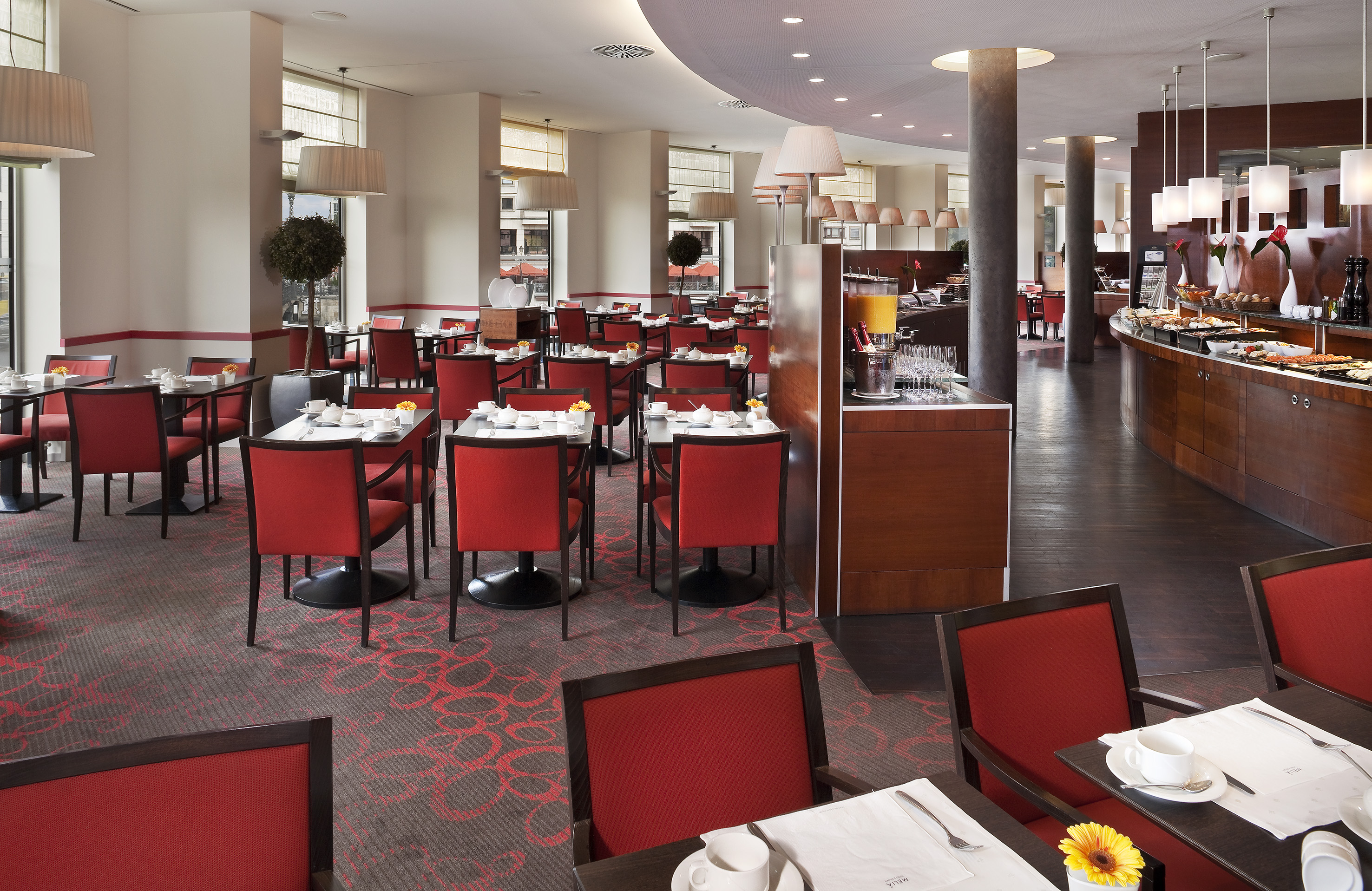 Hotel restaurant dining area with red chairs, set tables, and breakfast buffet. - Ontbijtbuffet, Show cooking - Meliá Berlin, Berlijn