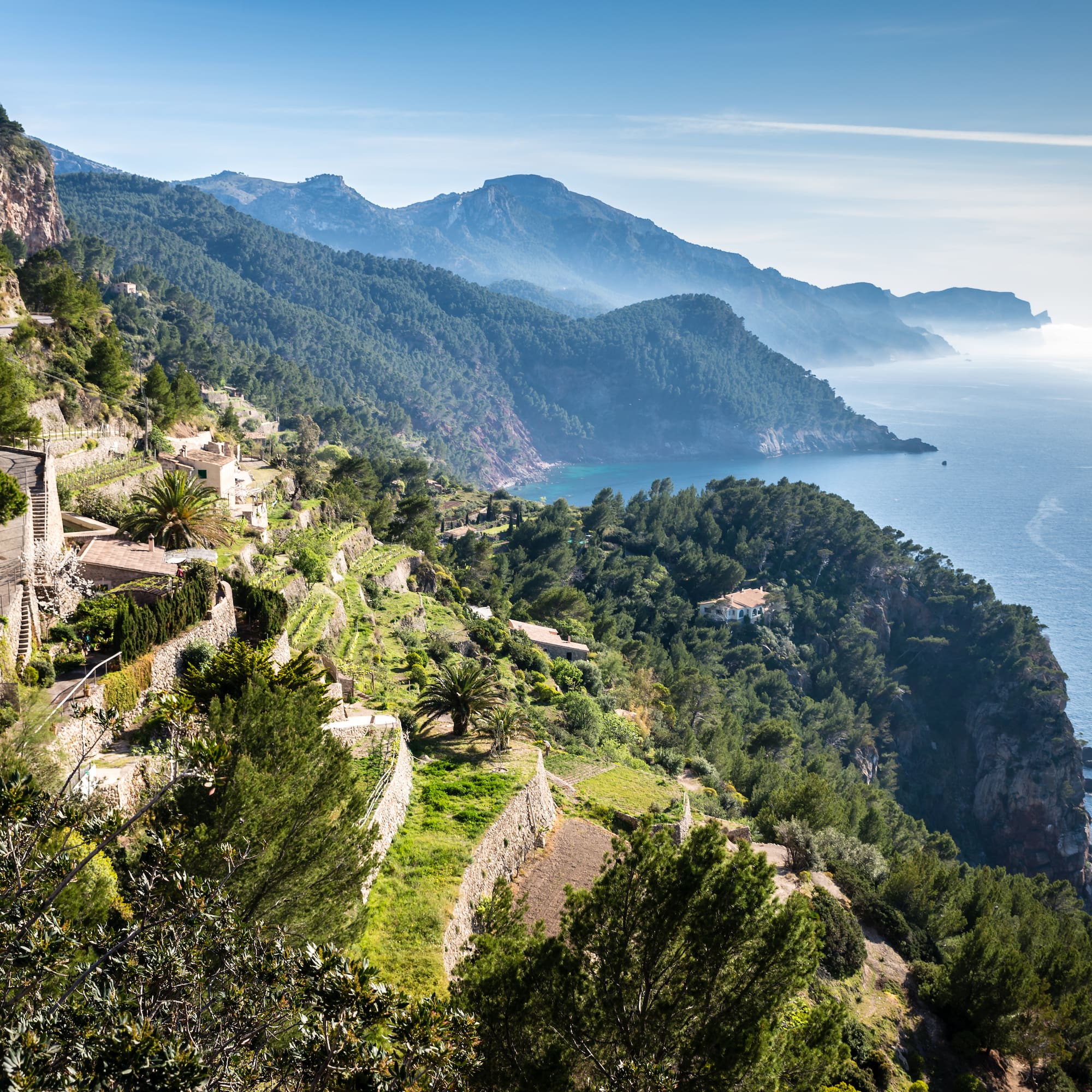 Terraced Mediterranean coast with a winding road, green hills, and blue sea.