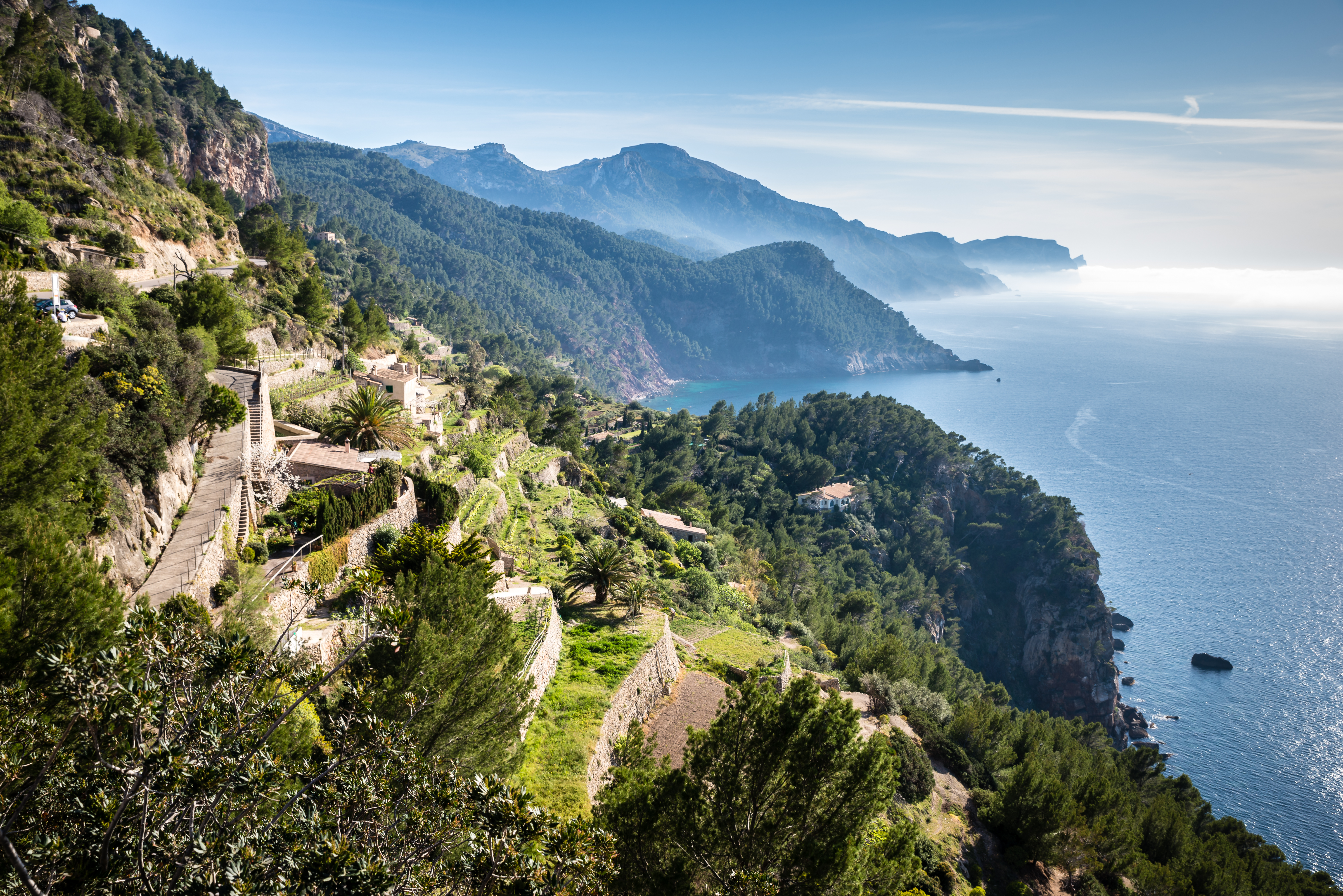 Terraced Mediterranean coast with a winding road, green hills, and blue sea.