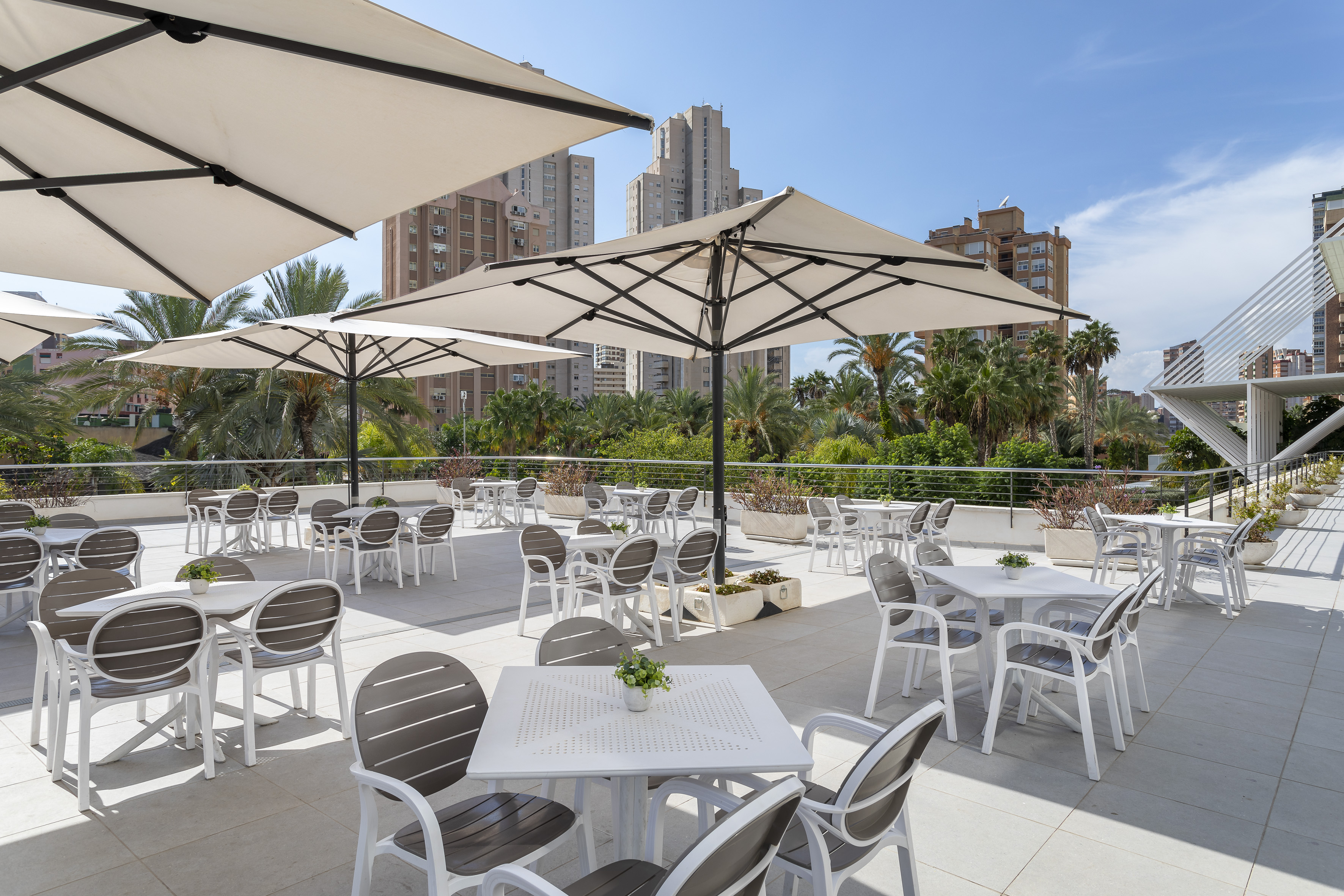 Outdoor terrace with dining tables, chairs, and umbrellas, overlooking city buildings.