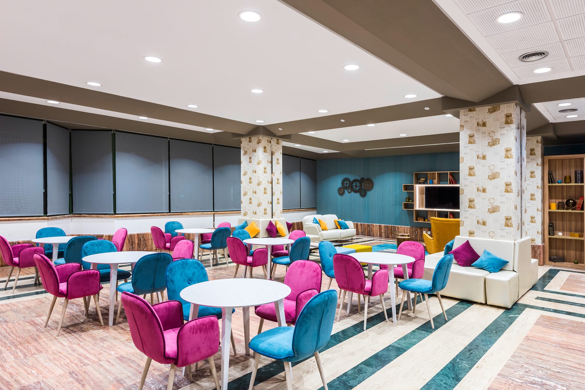 Modern lounge interior with colorful pink and teal chairs and white tables.