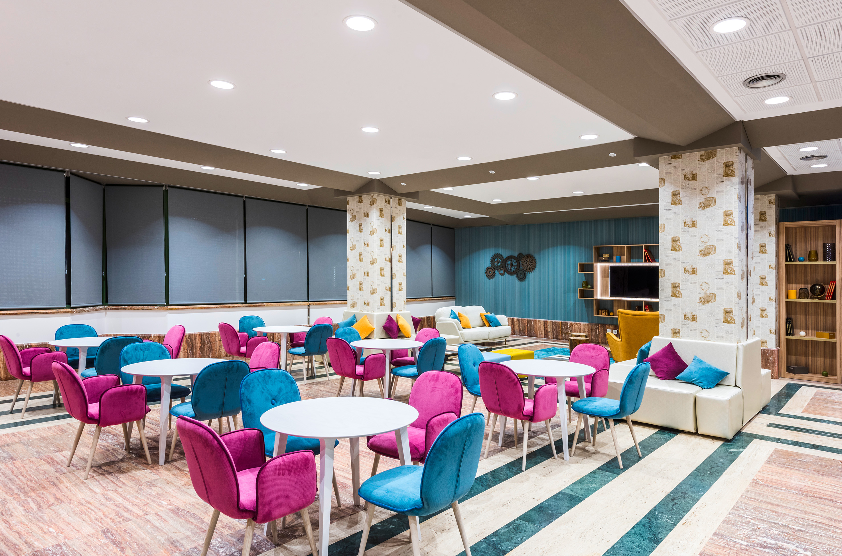 Modern lounge interior with colorful pink and teal chairs and white tables.