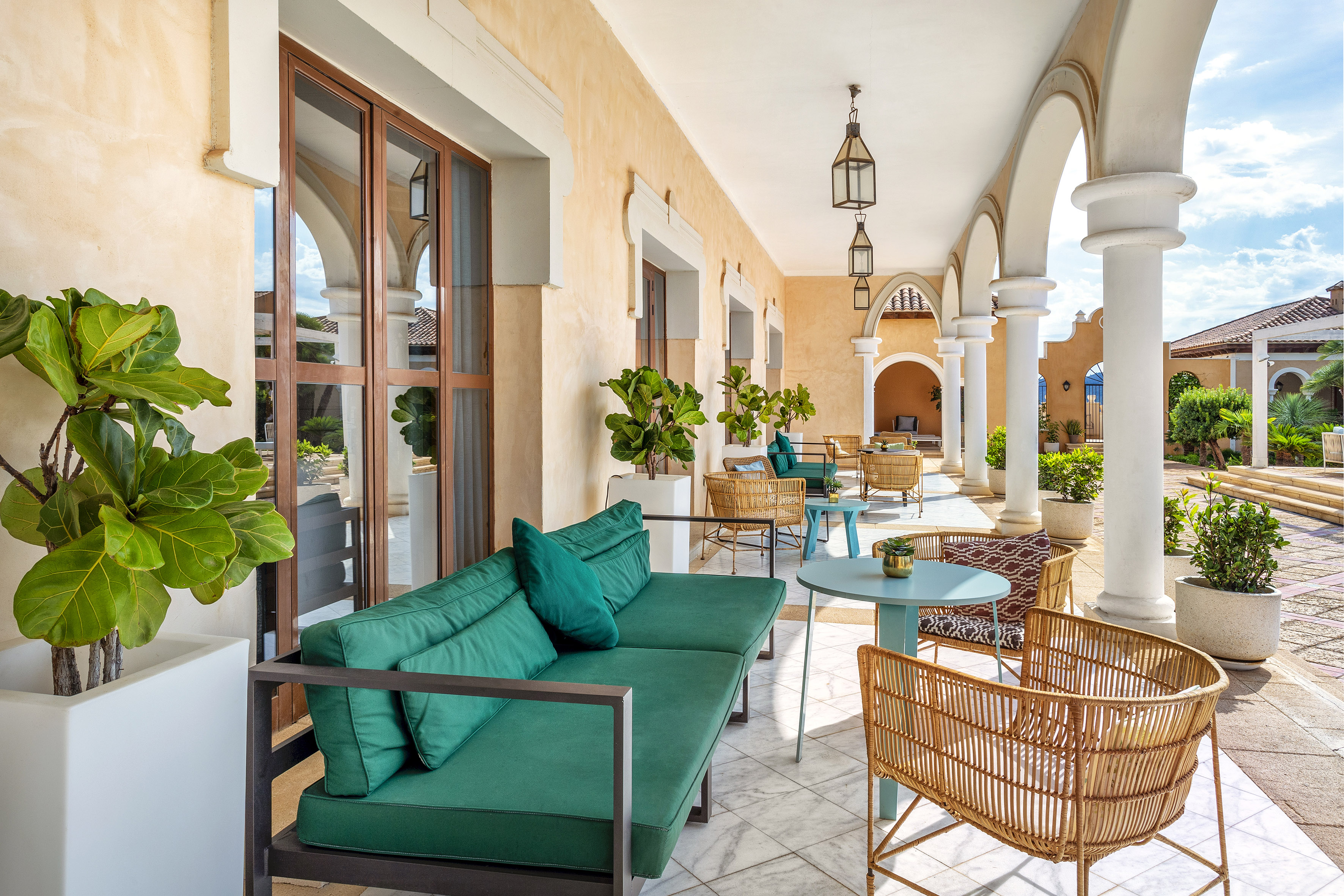 Luxurious outdoor patio with green sofa, wicker chairs, arches, and plants.