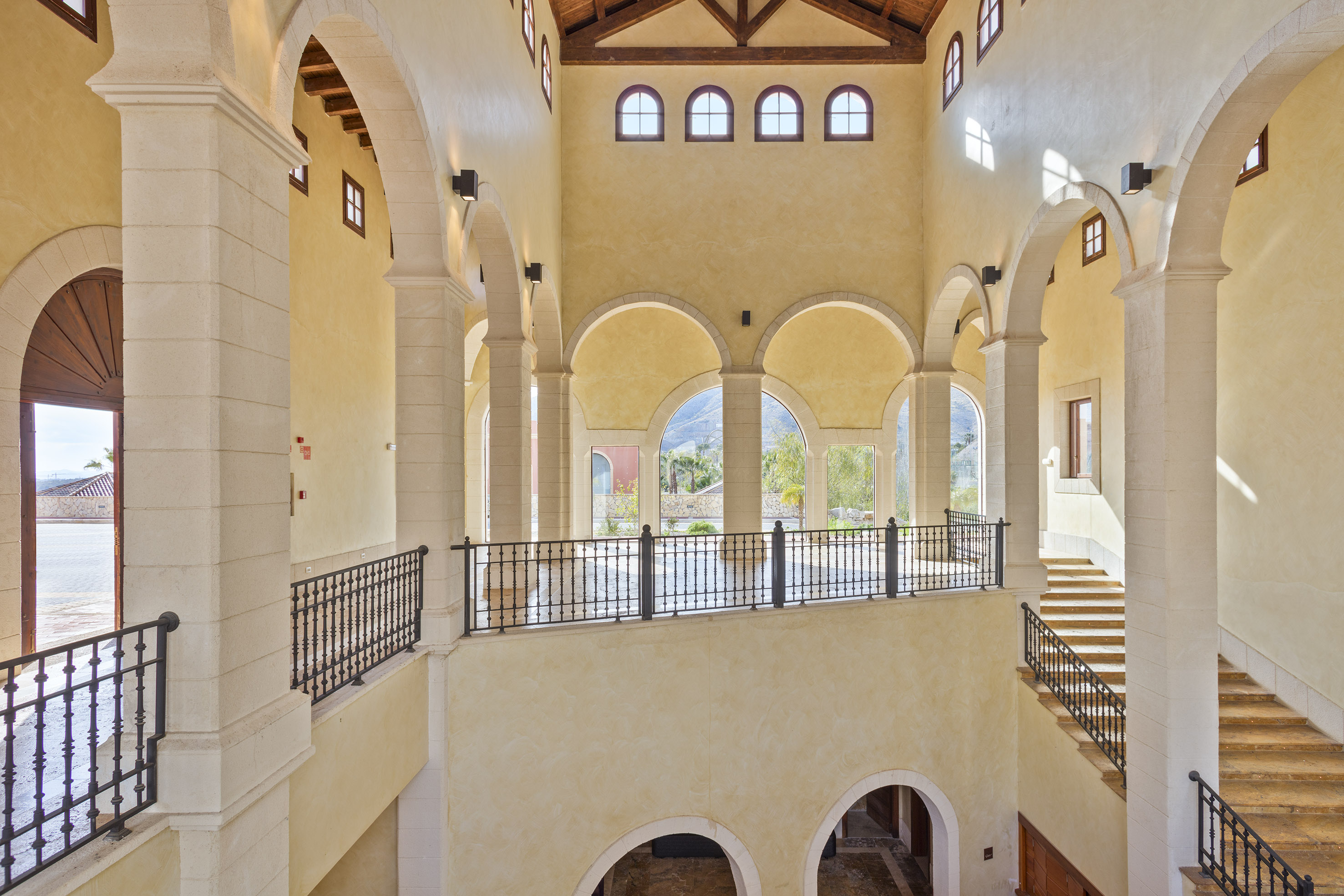 Grand Mediterranean hall with arches, columns, wrought iron, and outdoor views.