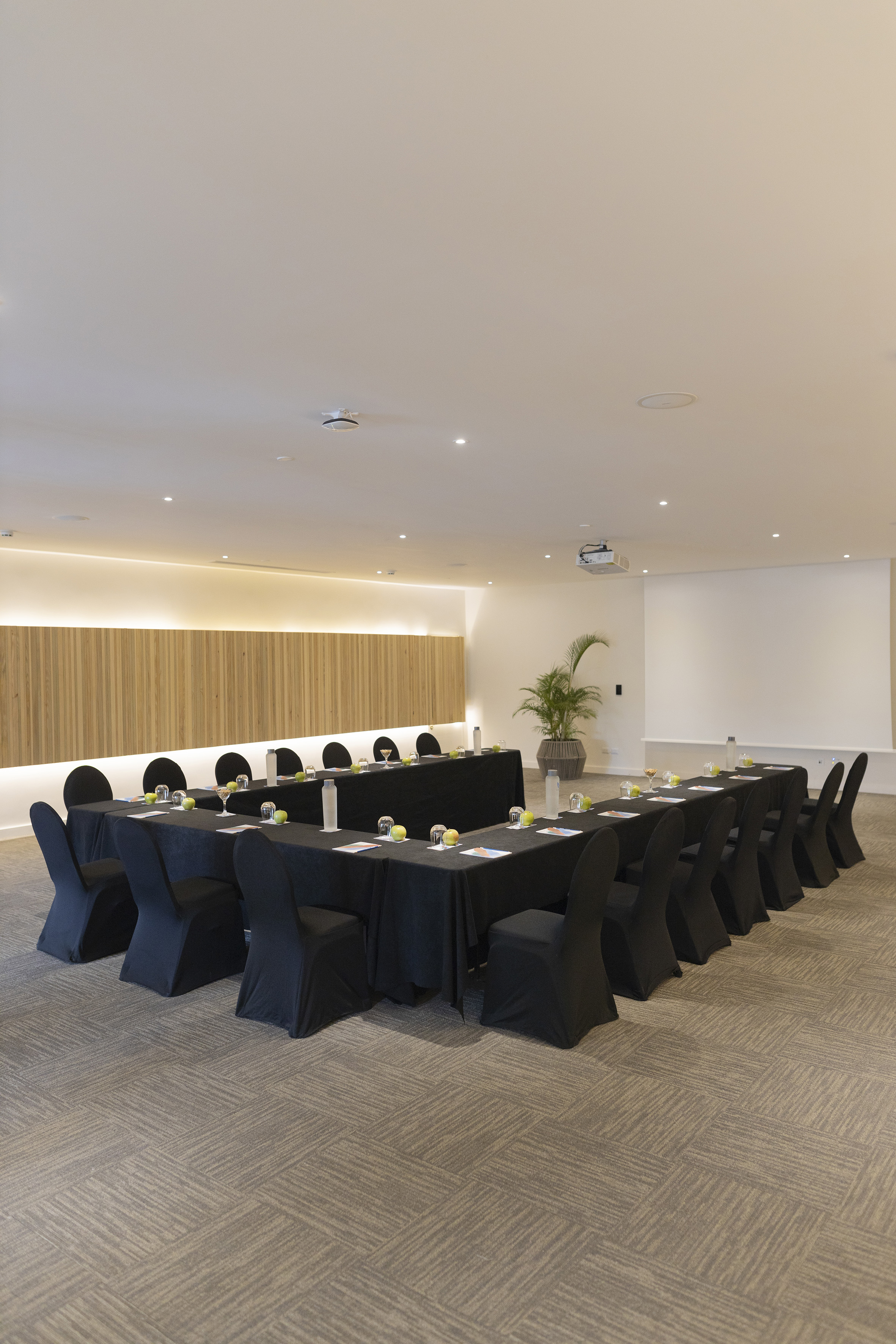 Modern U-shaped meeting room with black tables, chairs, projector, and wood accent.