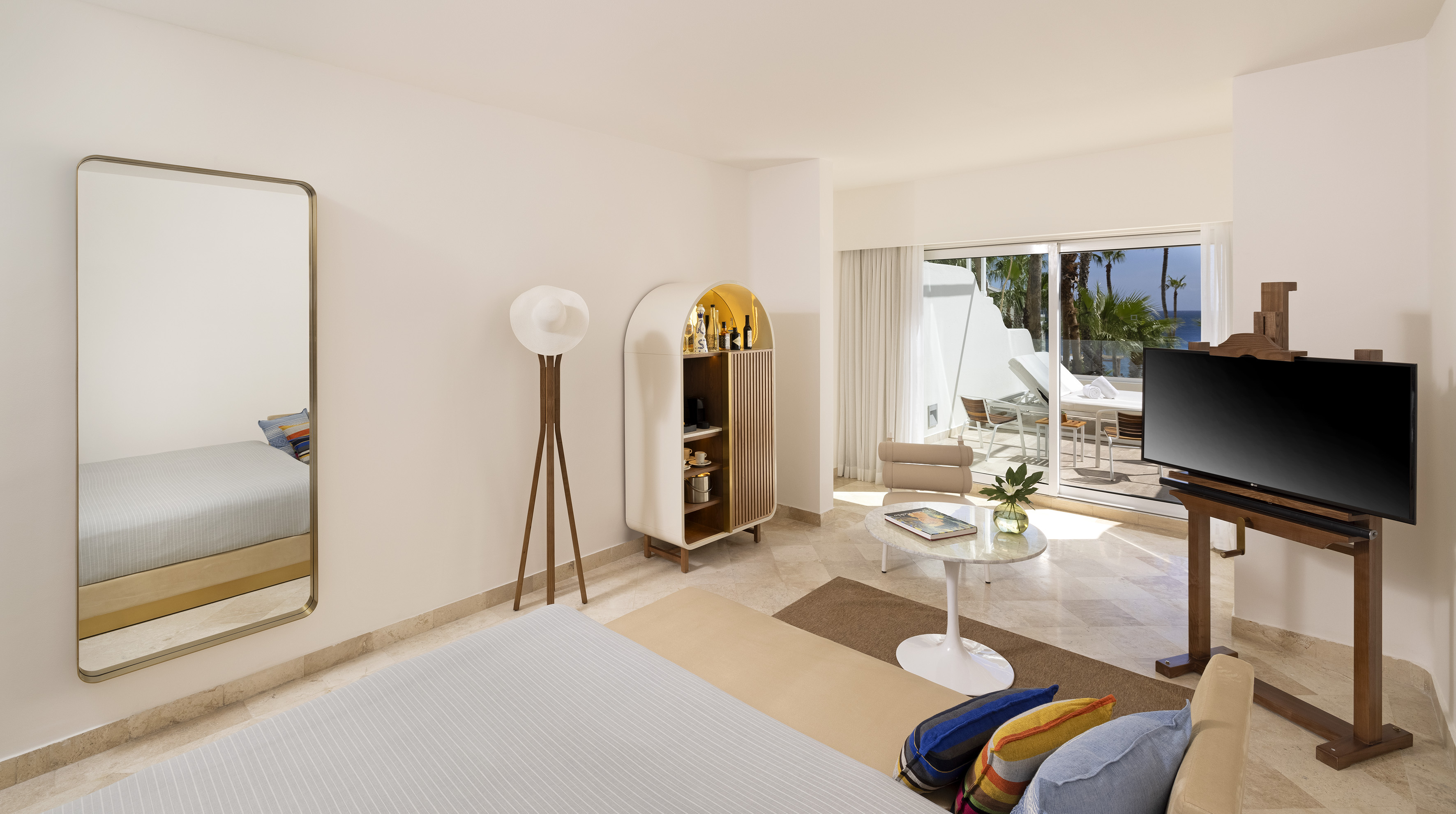 Modern hotel suite with ocean view balcony, TV, and stylish minibar.