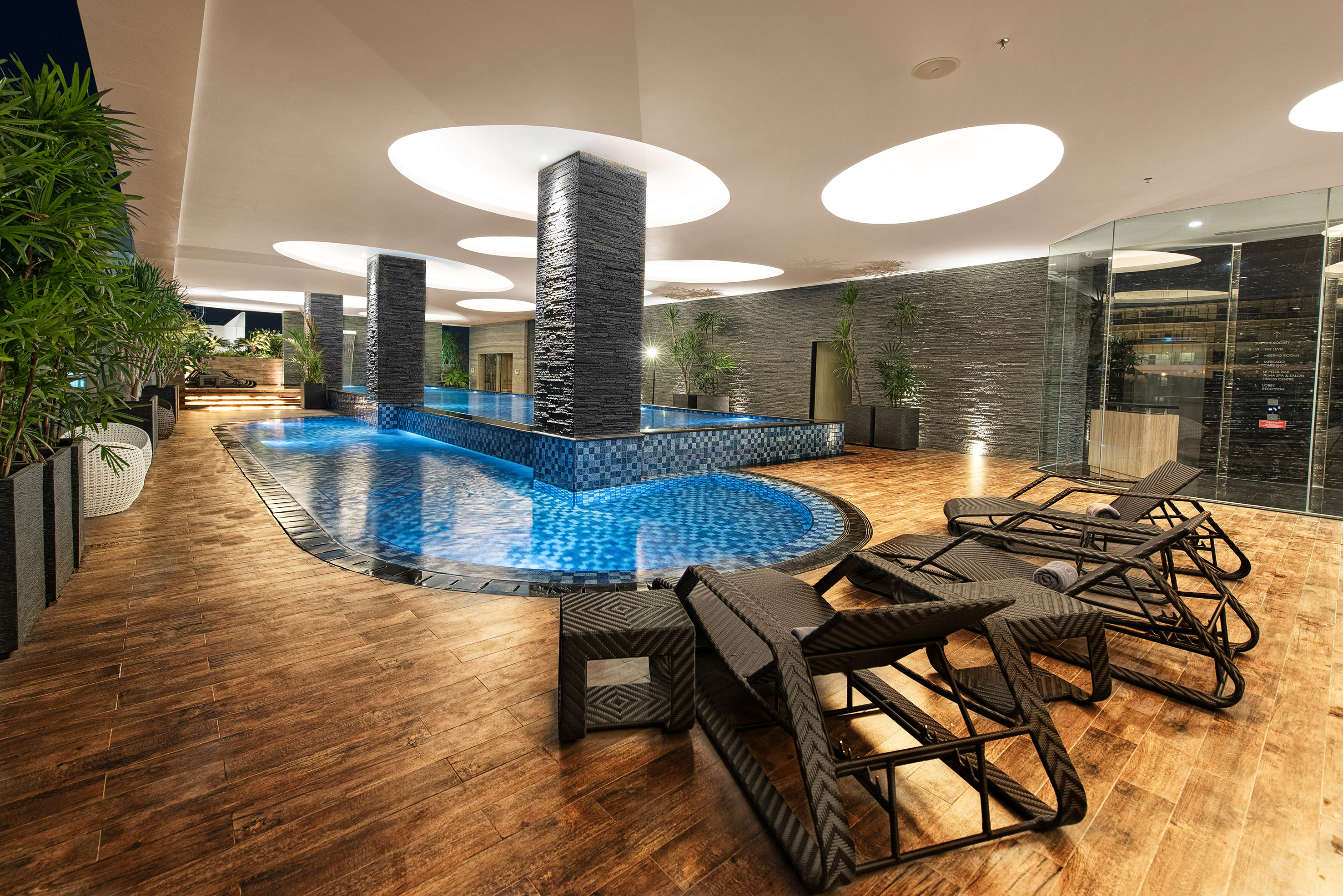 Luxury indoor pool with modern design, lounge chairs, and wooden floor.
