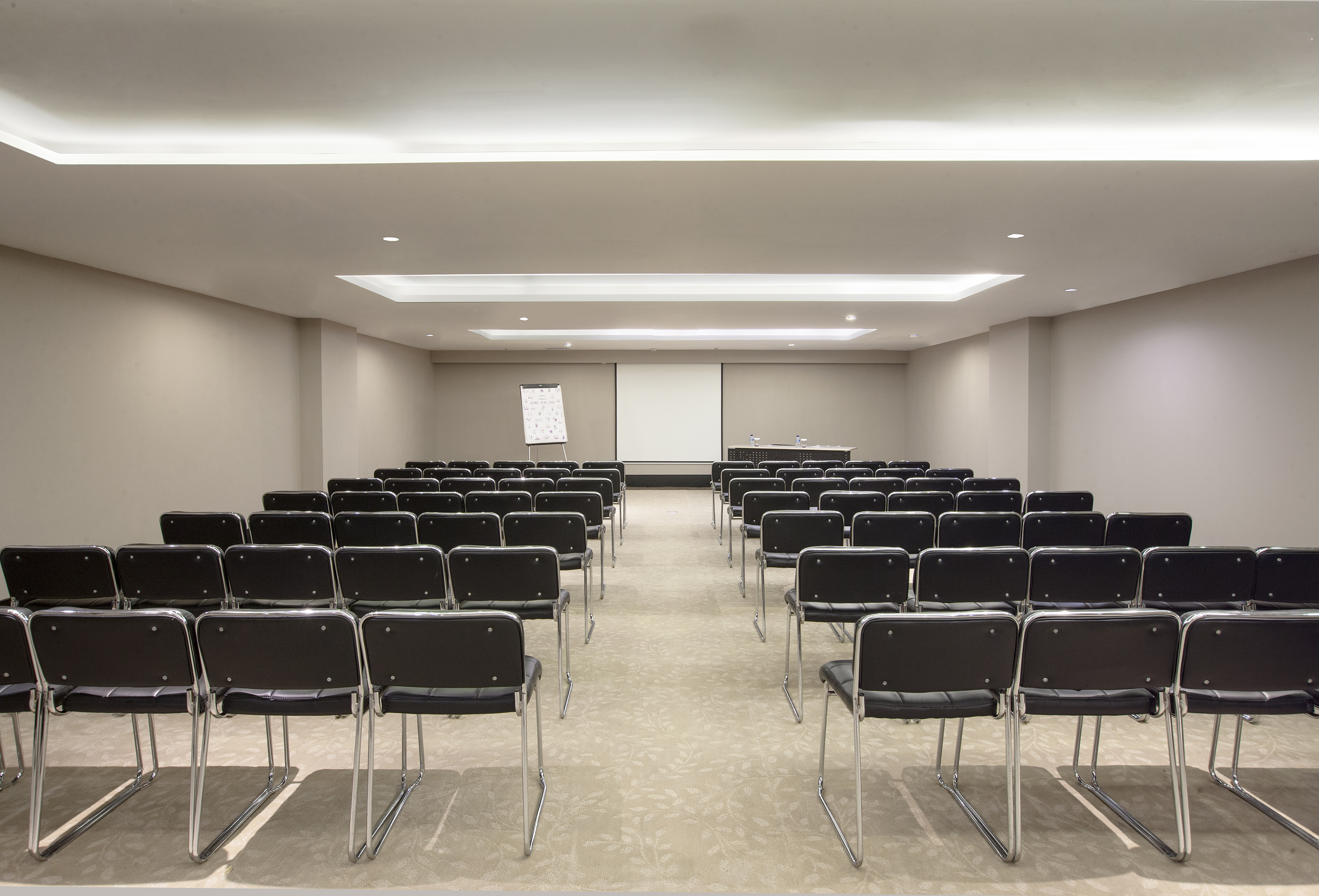 Empty conference room with rows of chairs, projector screen, and flip chart.