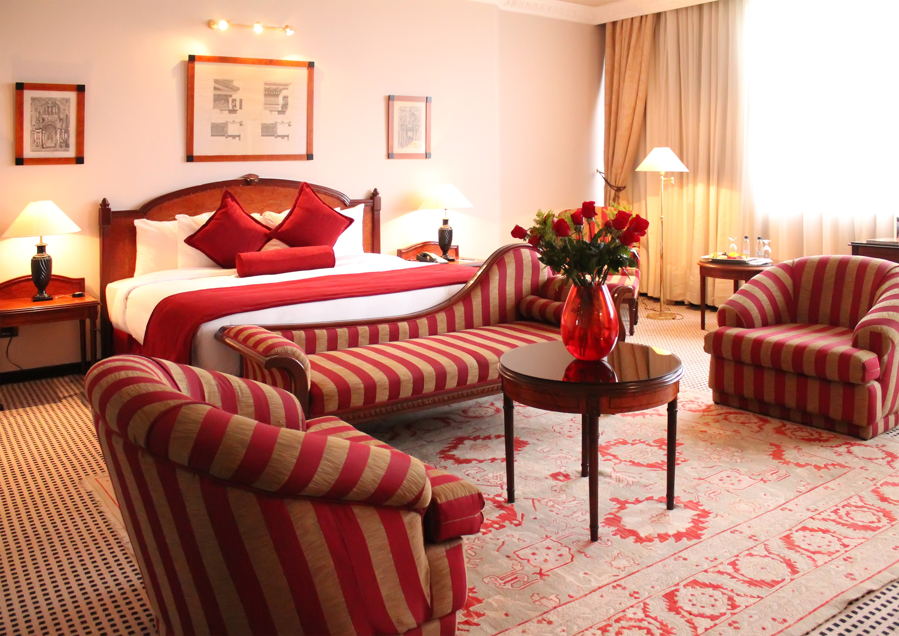 Luxury hotel suite with red and gold striped furniture, bed, and roses.