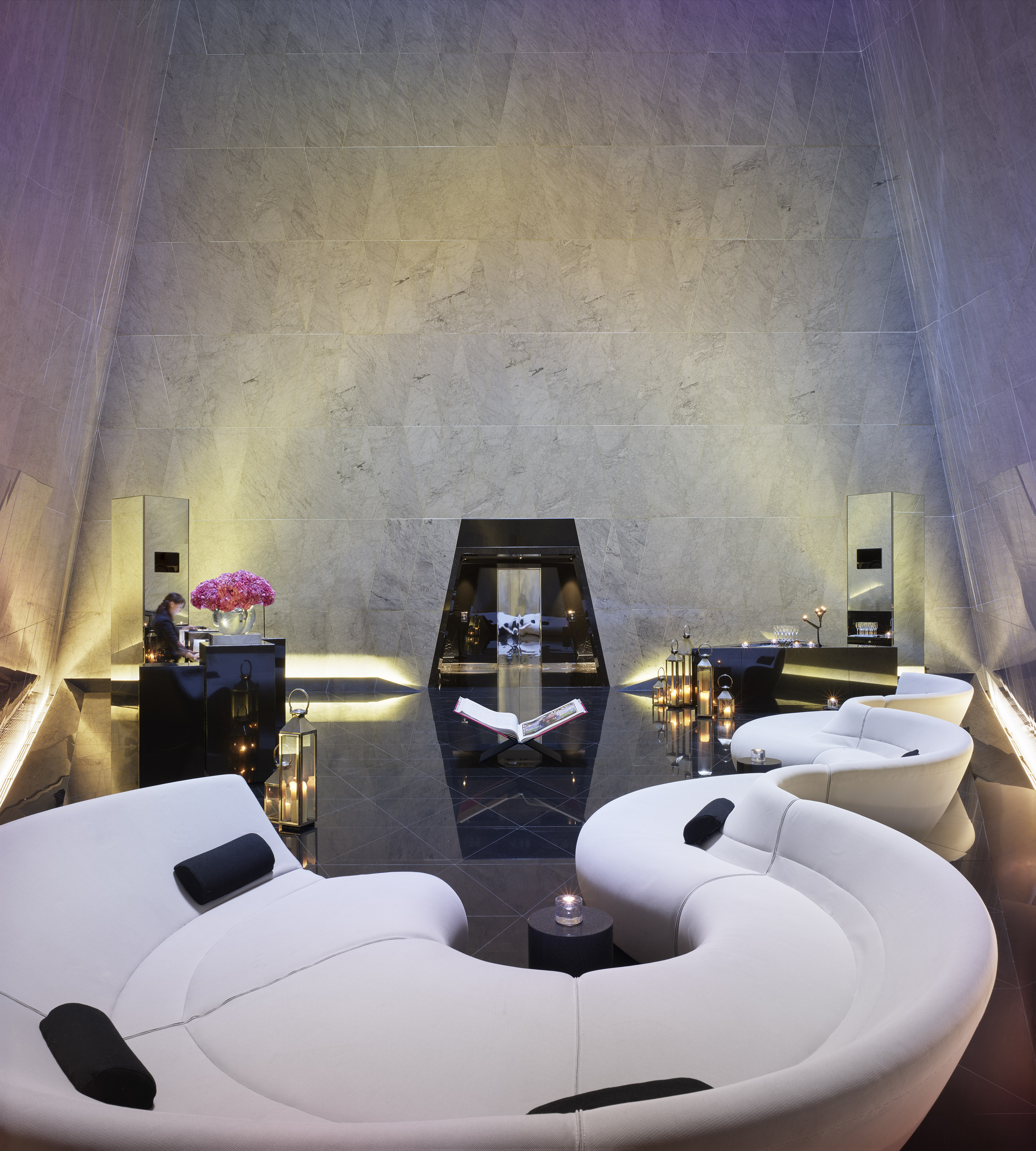 Chic modern hotel lobby with white modular seating, marble walls, ambient lighting.