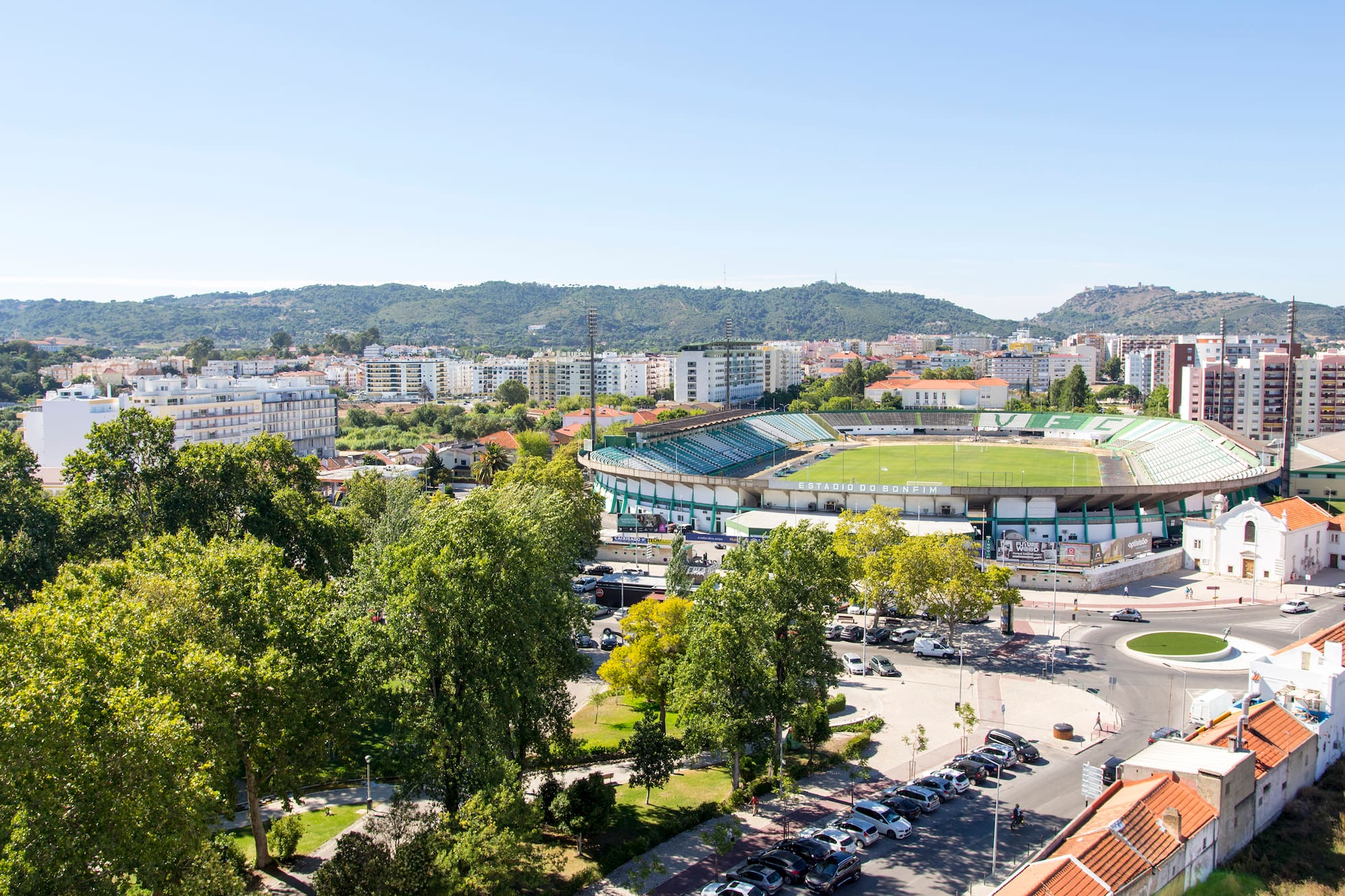 Estádio do Bonfim stadium in Setúbal, Portugal, with city buildings and mountains.