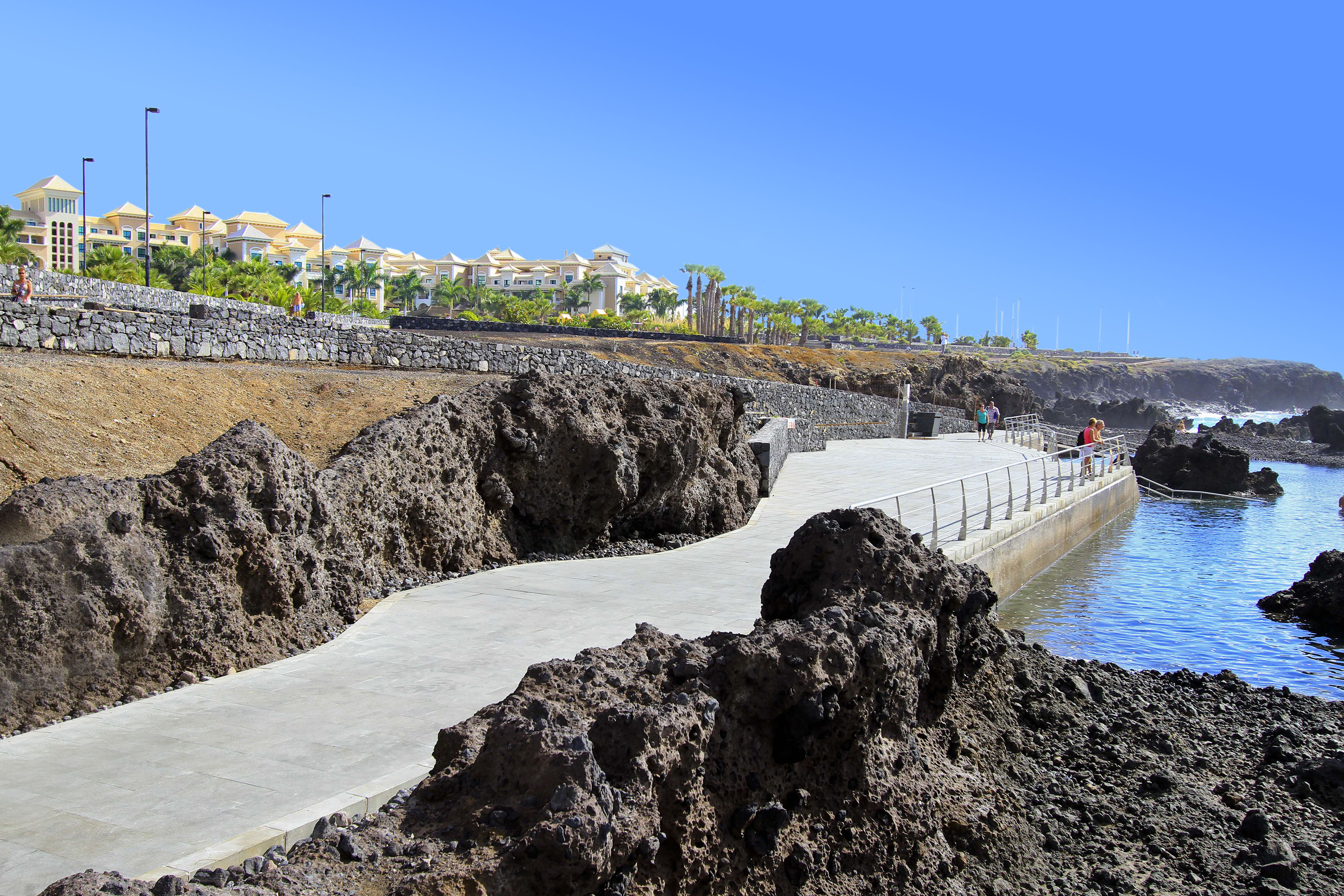 Coastal promenade along volcanic coastline with distant hotels and blue ocean.