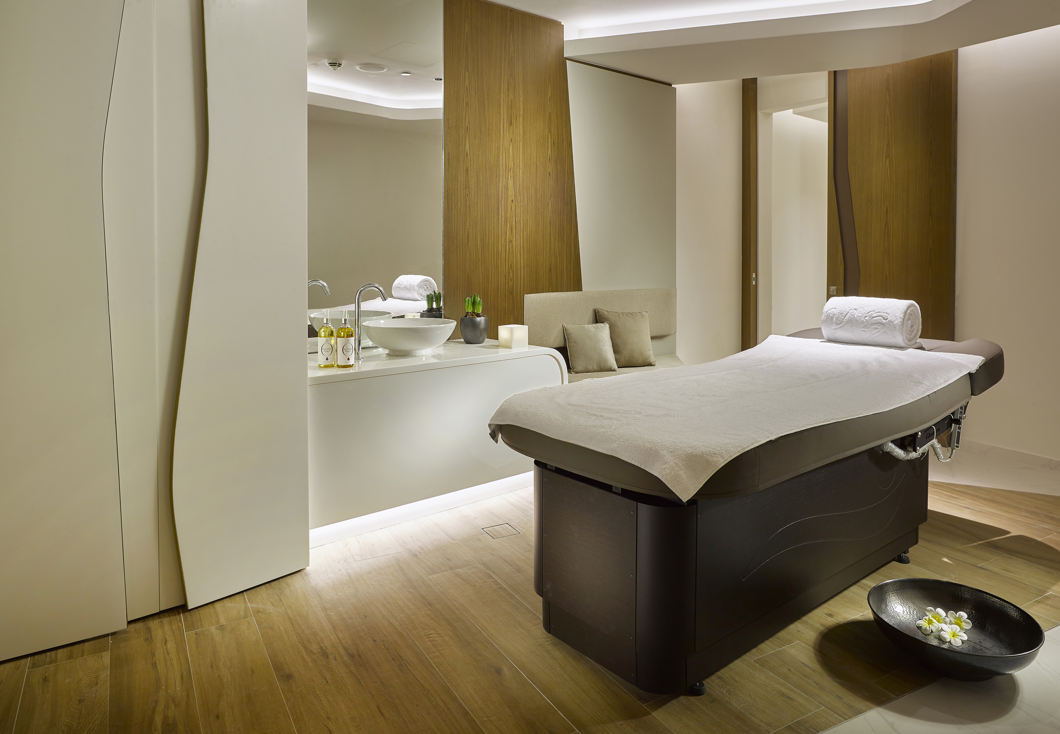 Modern spa treatment room with massage table, white towels, and vanity.