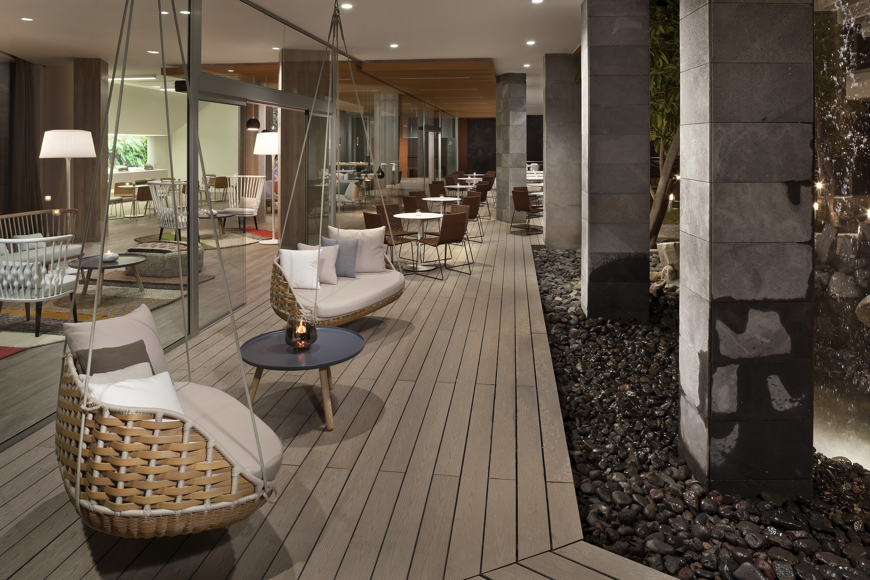 Modern outdoor cafe patio with hanging woven chairs and wooden deck.