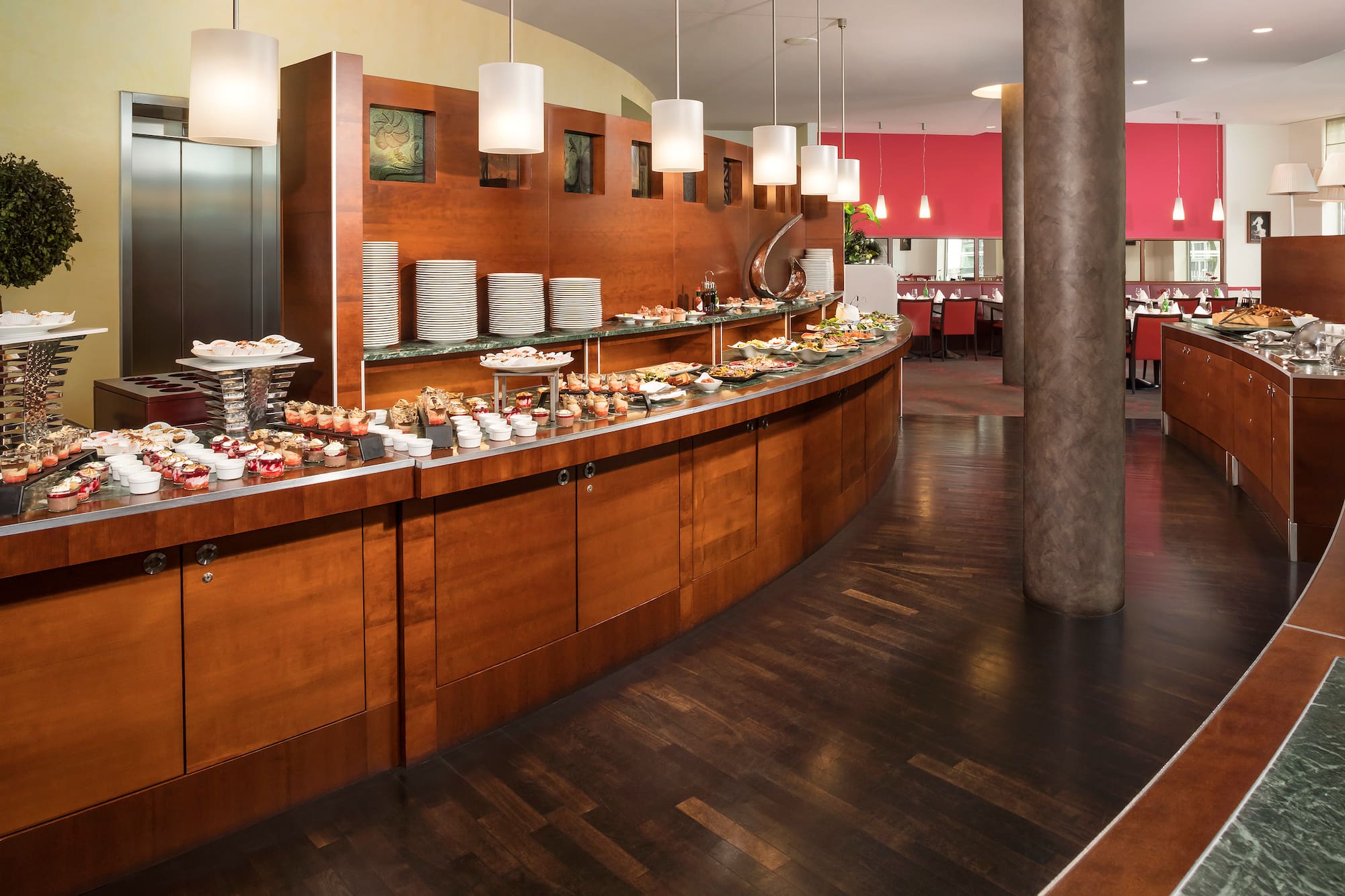 Modern hotel buffet with diverse food, desserts, plates, and restaurant seating.