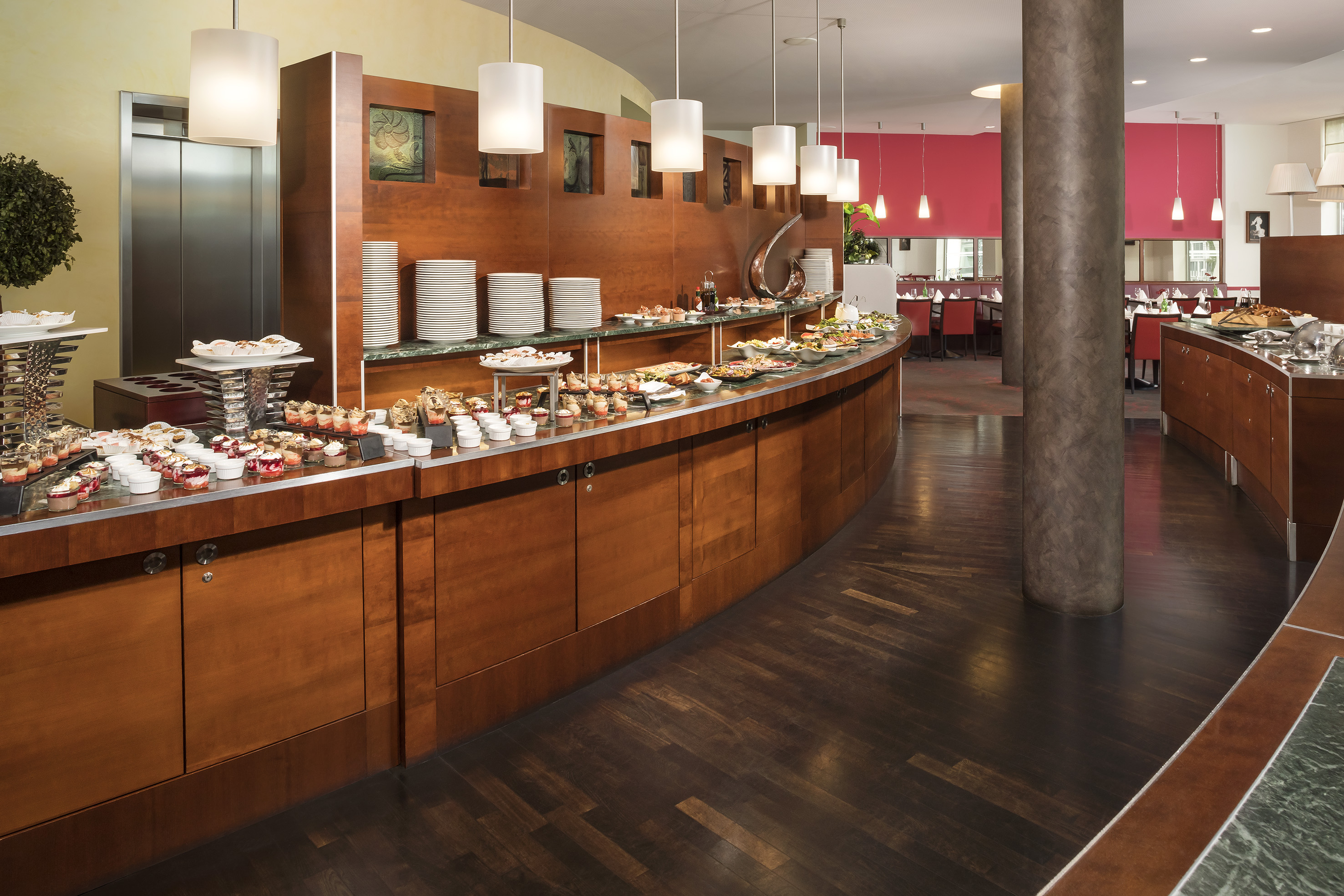 Modern hotel buffet with diverse food, desserts, plates, and restaurant seating.
