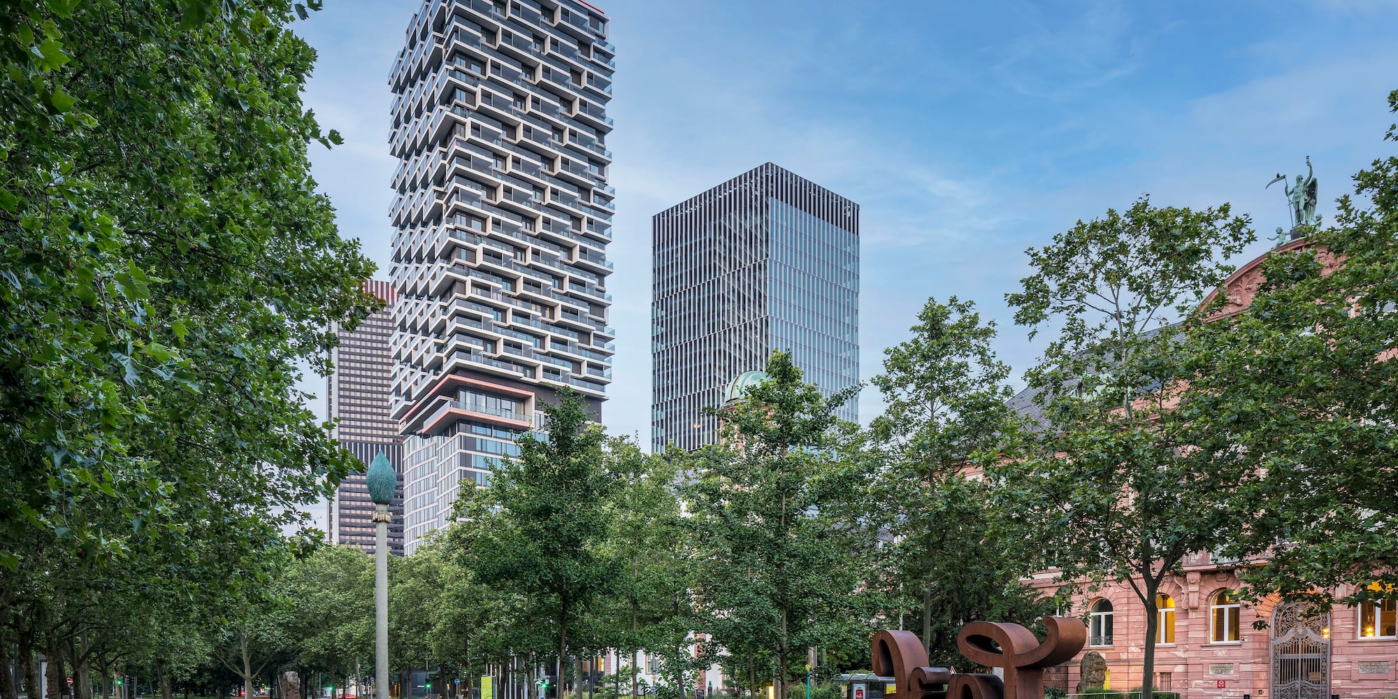 a park with trees and a sculpture in front of a tall building