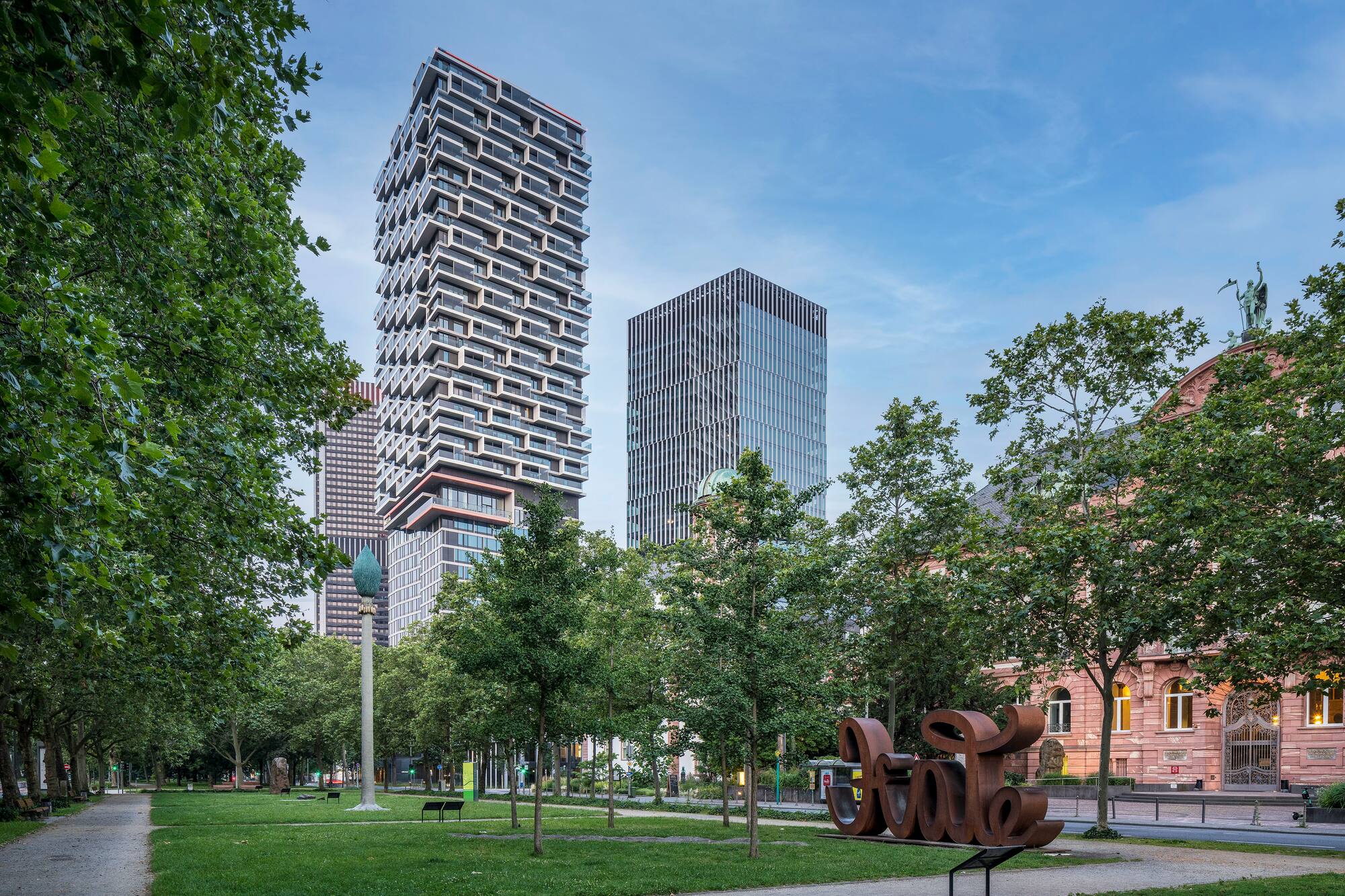 Frankfurt city park with modern skyscrapers, green trees, and Städel sculpture.