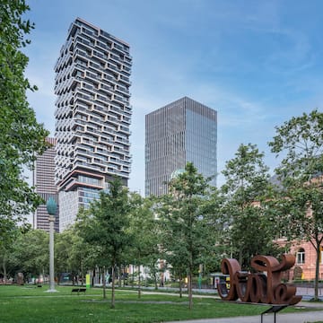 a park with trees and a sculpture in front of a tall building