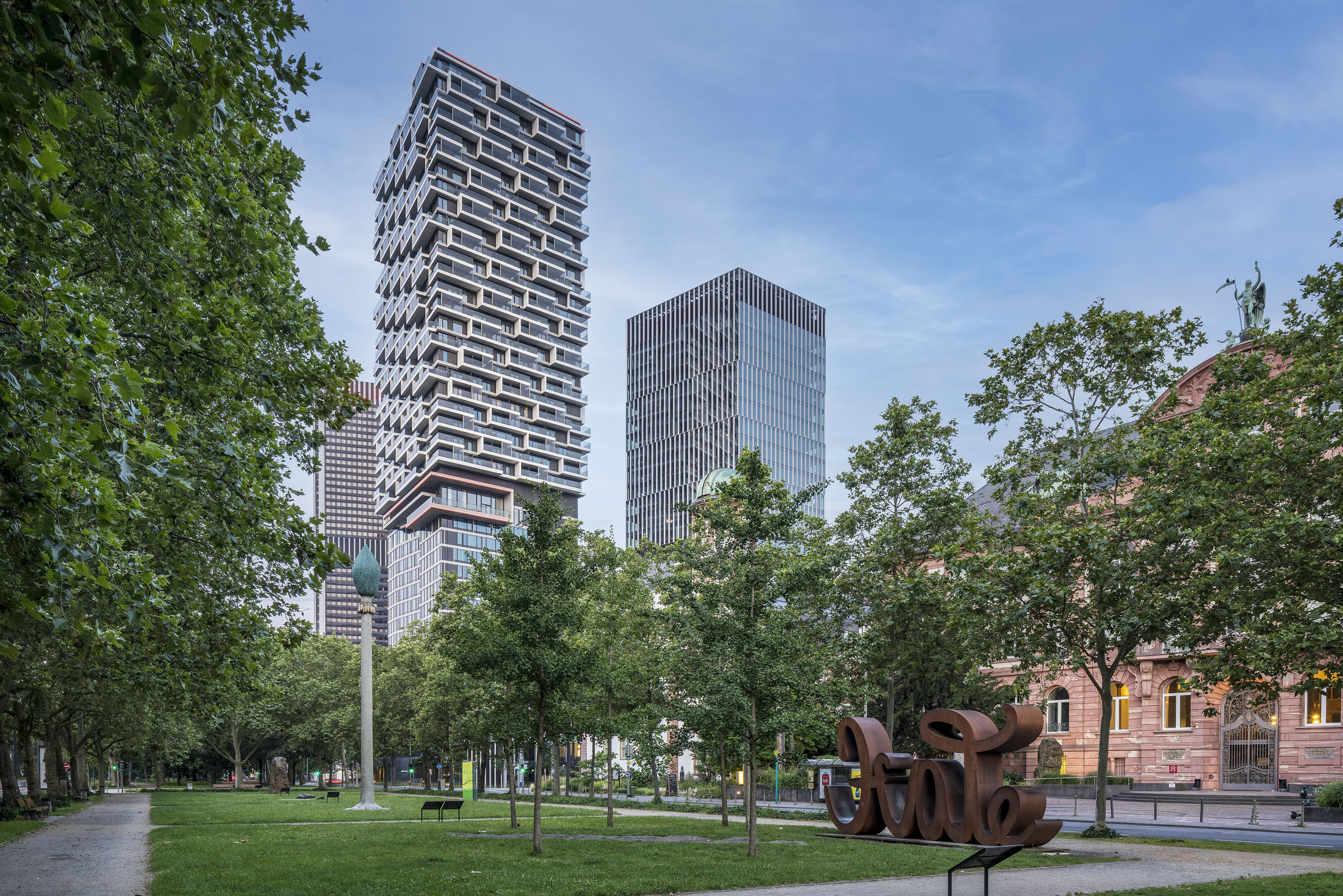 a park with trees and a sculpture in front of a tall building