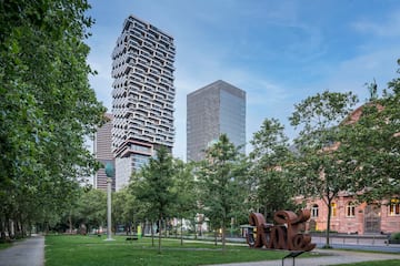 a park with trees and a sculpture in front of a tall building