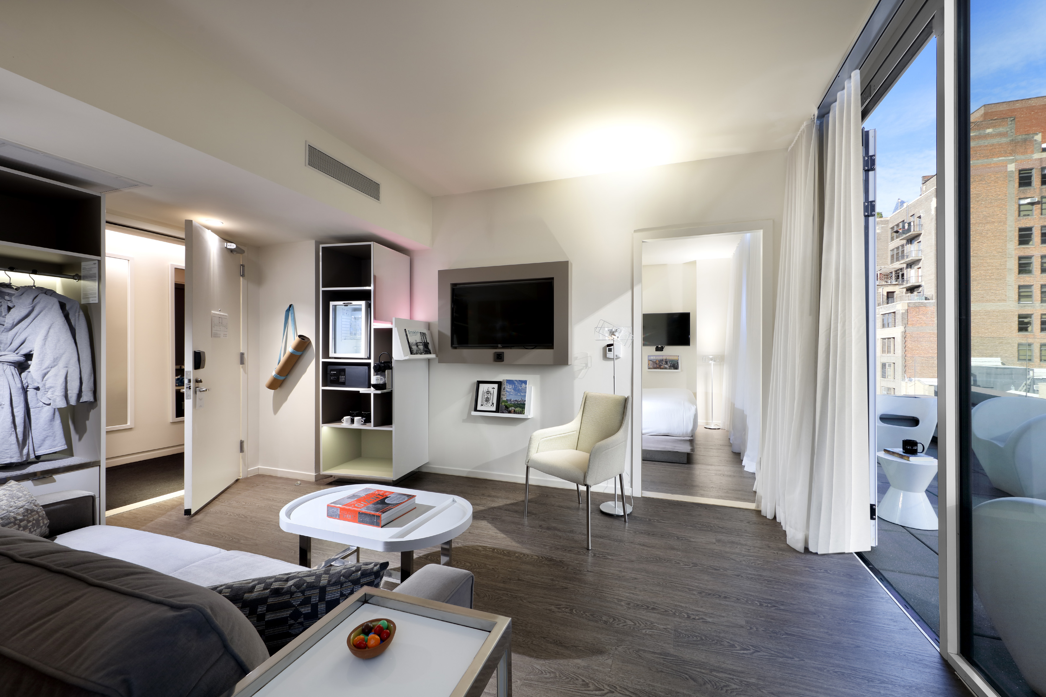 Modern hotel suite: living room, TV, bedroom, and balcony with city view.