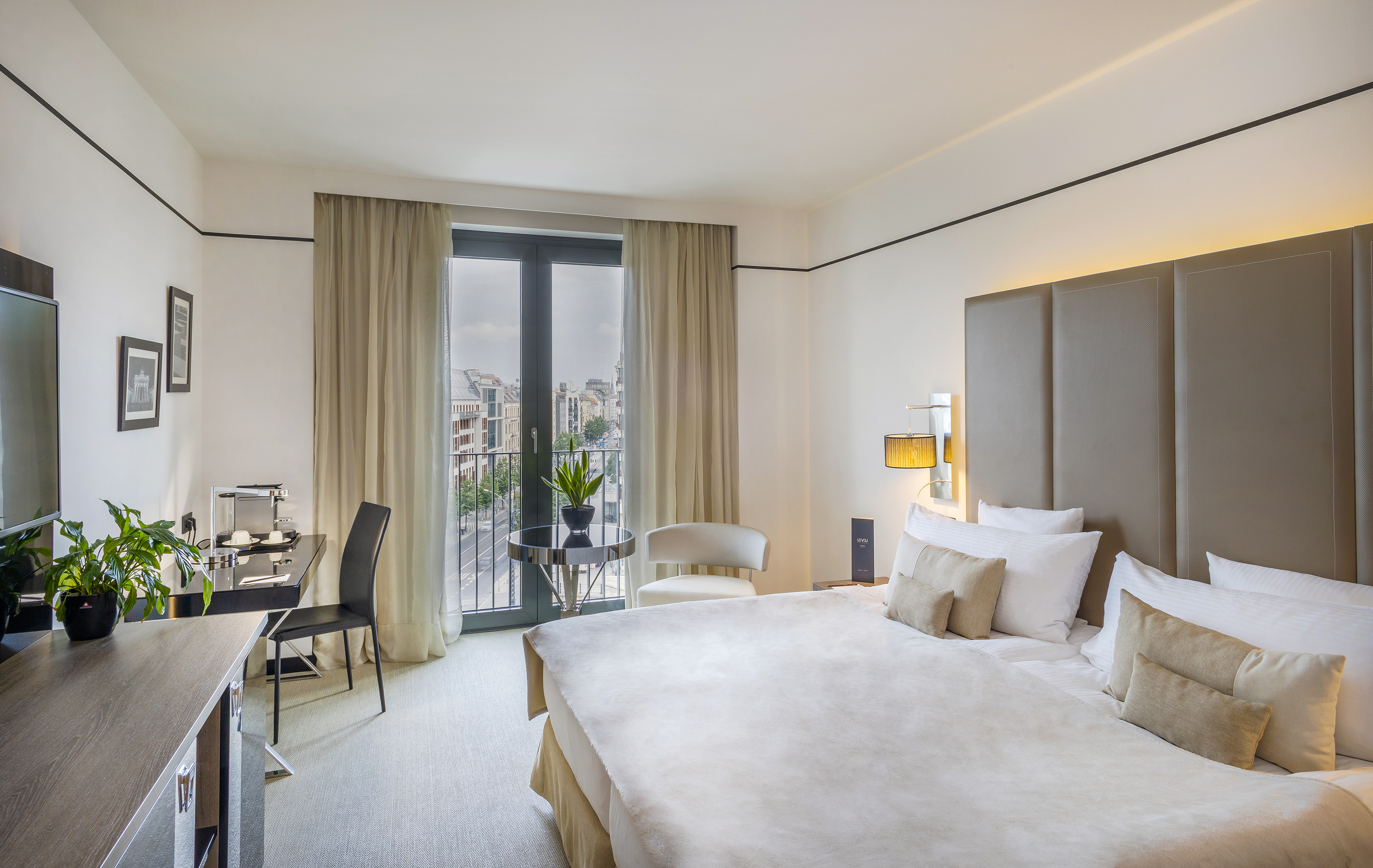 Modern hotel room with king bed, desk, city view balcony, and neutral decor.