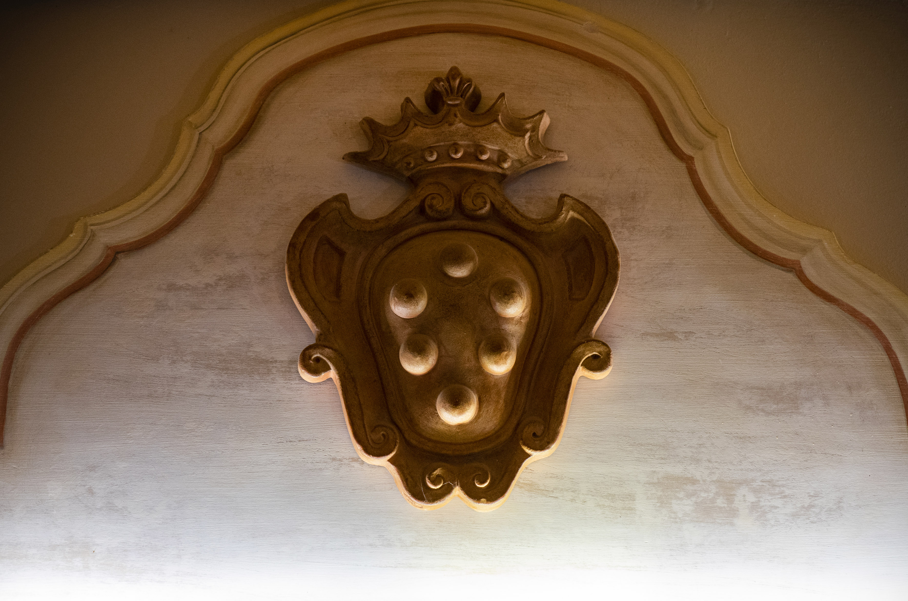 Ornate gold Medici crest with crown and six palle on a textured background.