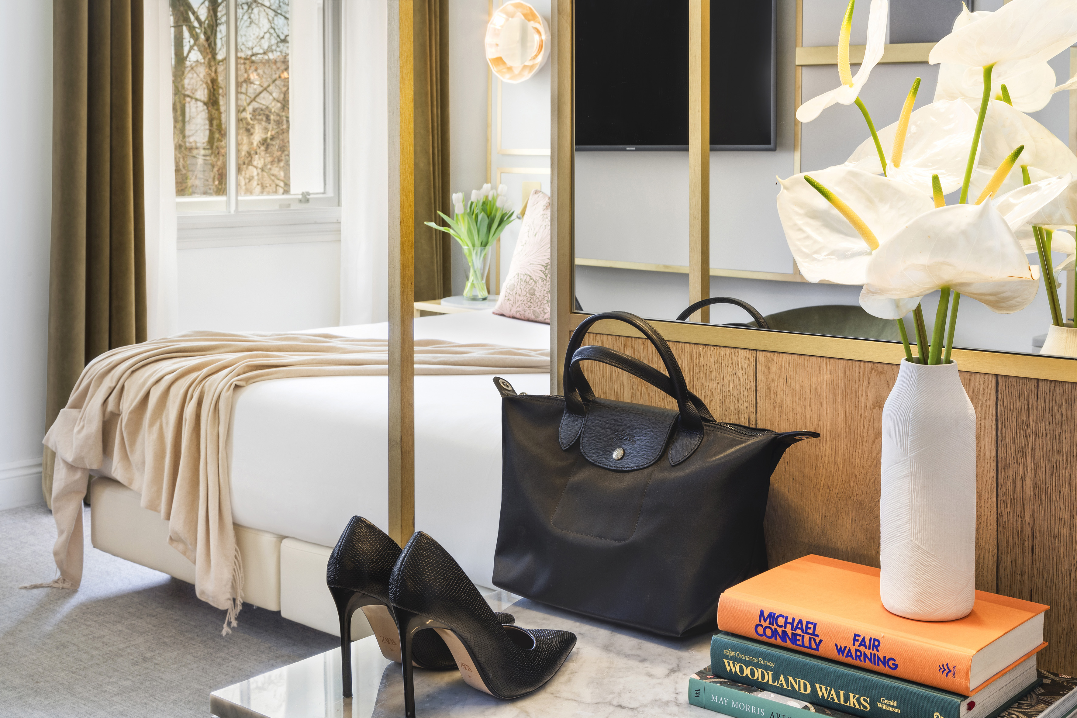 Luxury hotel room with black high heels, handbag, books, and white flowers.
