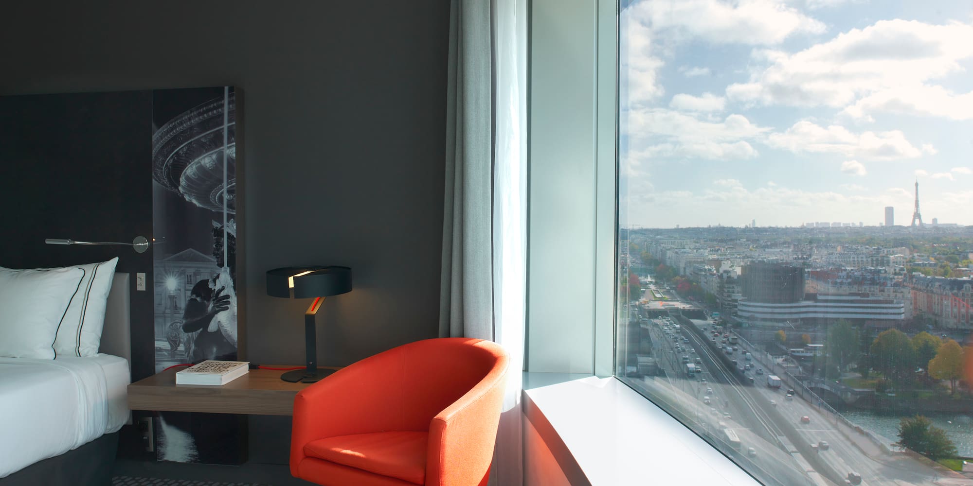 Modern hotel room with orange chair, panoramic Paris view & Eiffel Tower.