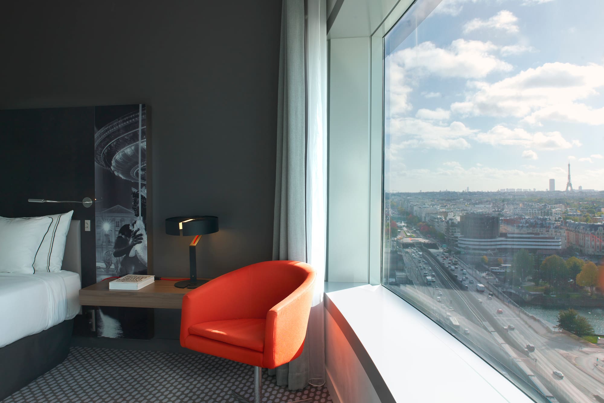 Hotel room with large window, city view of Paris and distant Eiffel Tower.