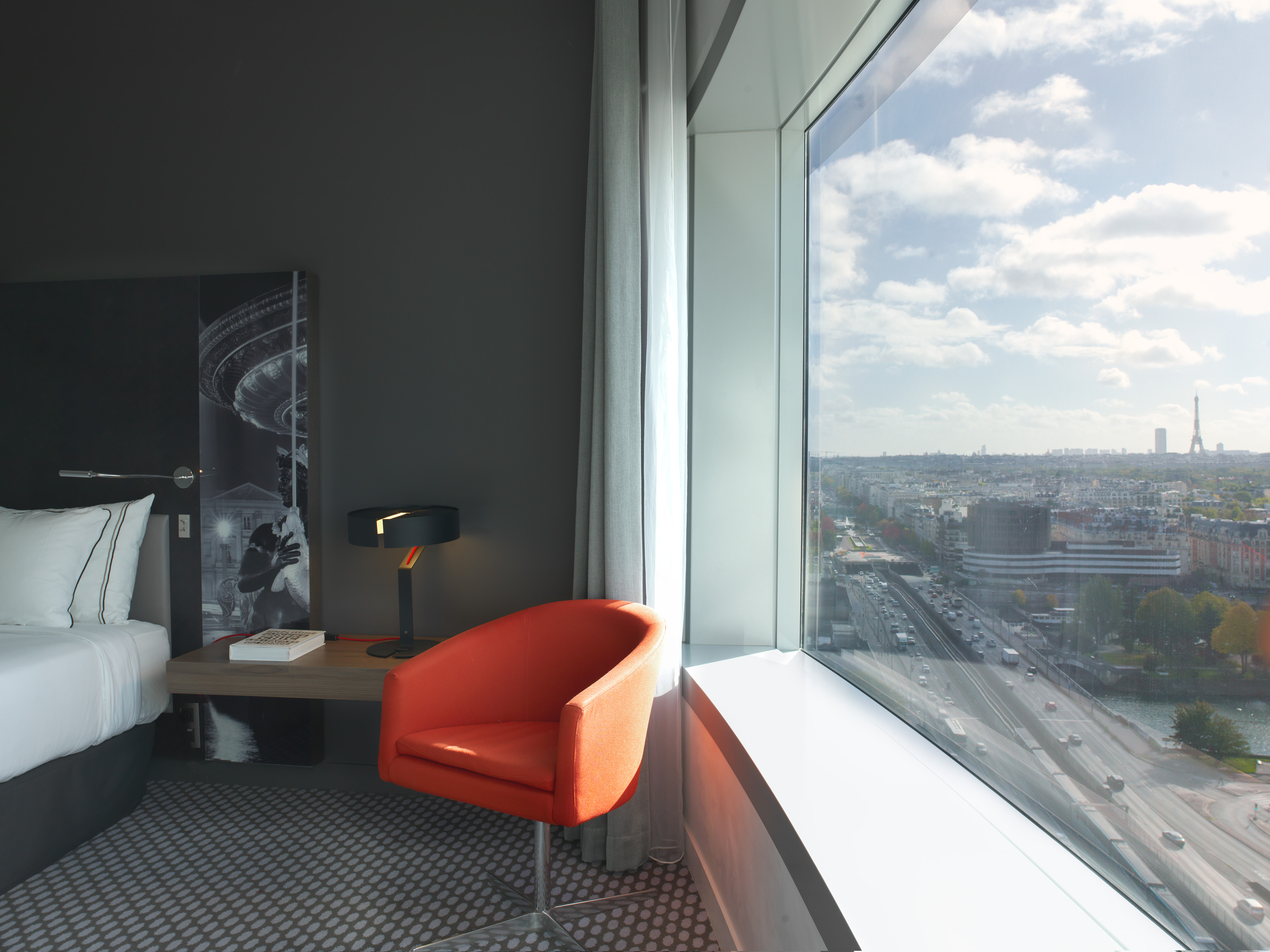 Modern hotel room with orange chair, panoramic Paris view & Eiffel Tower.