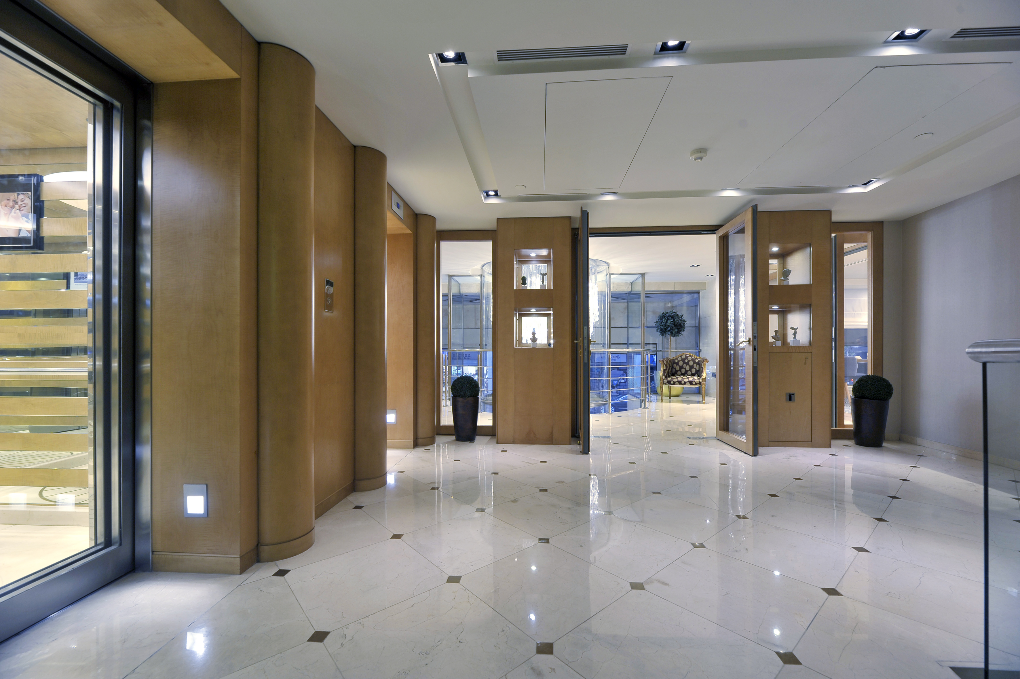 Luxury hotel lobby with wood panels, glass elevator, and polished marble floor.