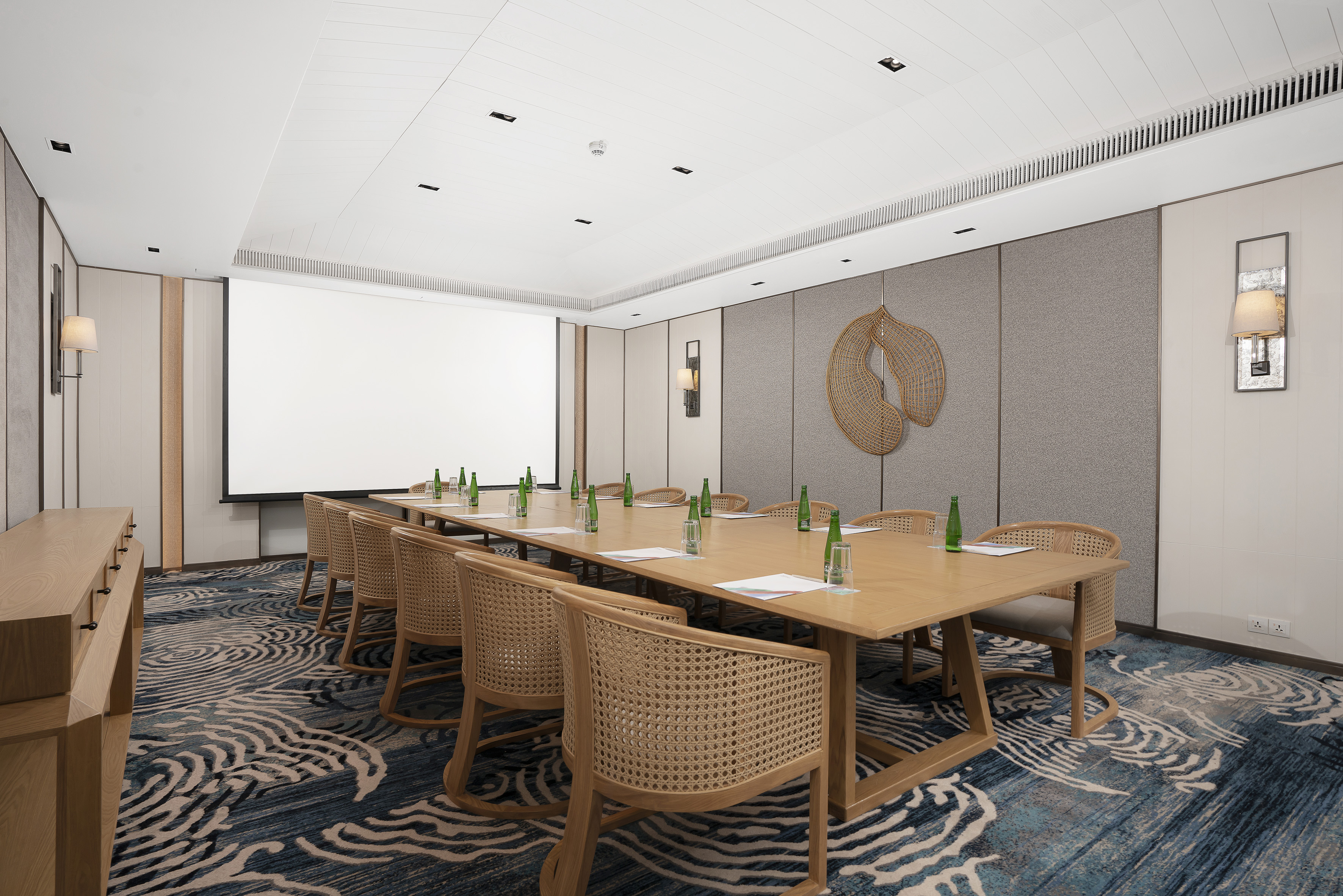 Modern conference room with wooden table, woven chairs, projector, and wave carpet.