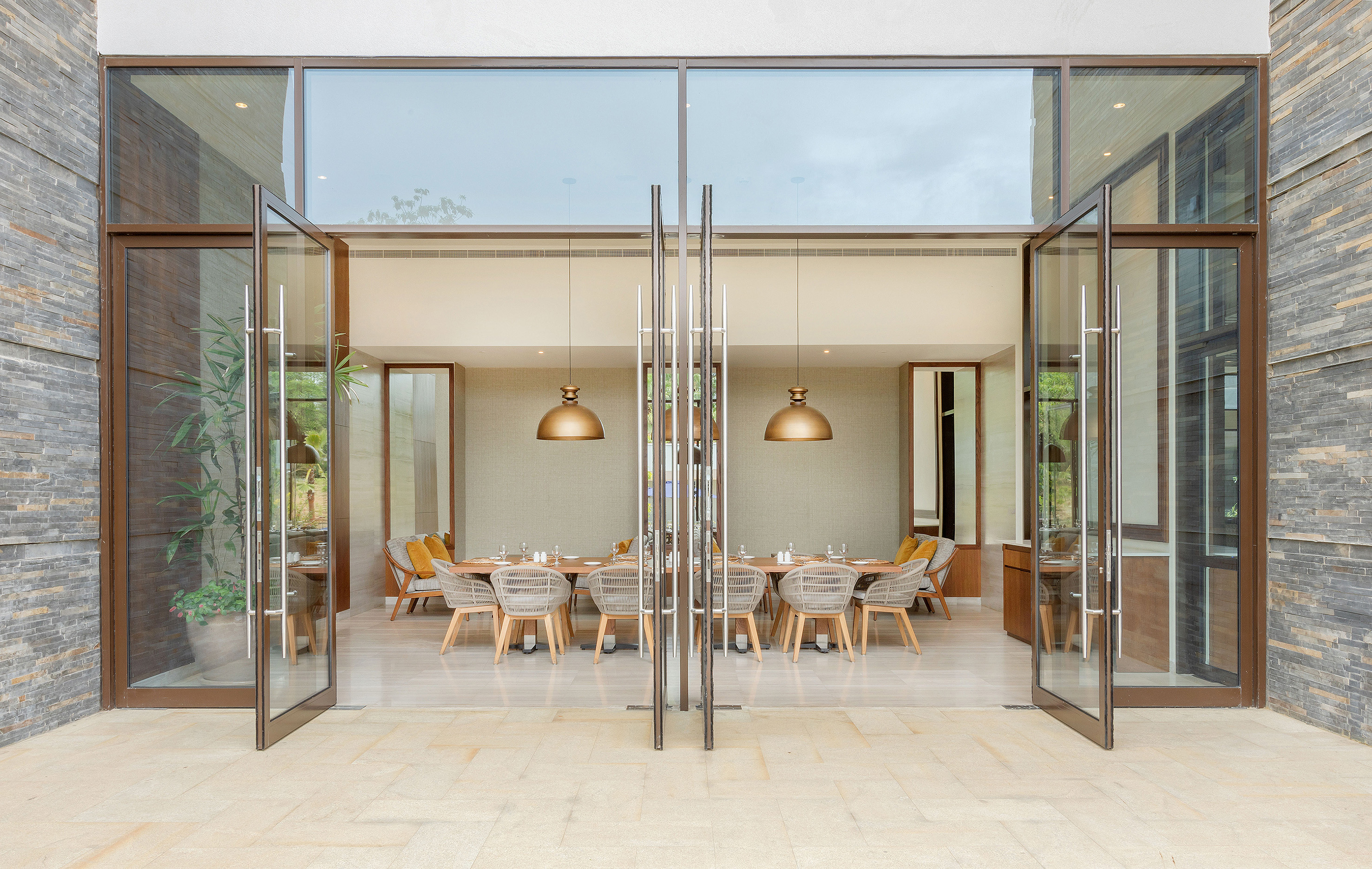 Luxury restaurant dining room through glass doors, flanked by stone walls.