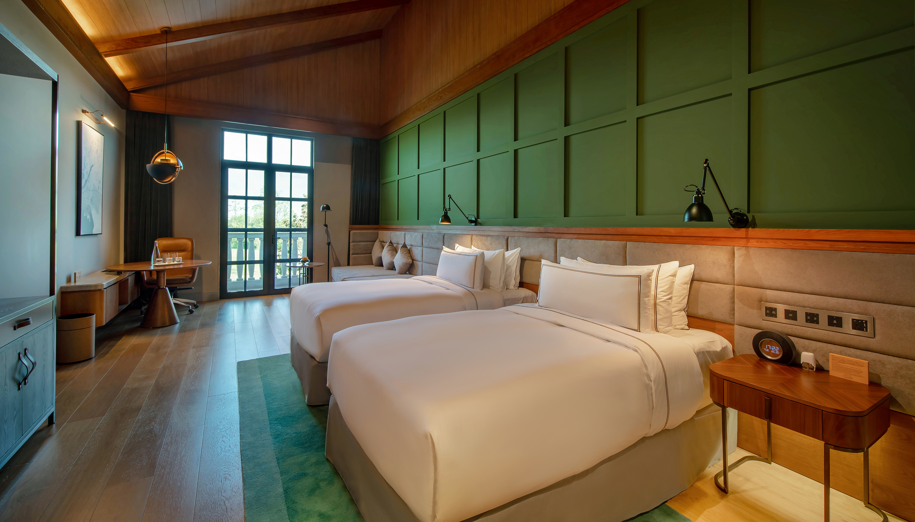 Luxury hotel room: twin beds, green paneled wall, vaulted wooden ceiling, desk.